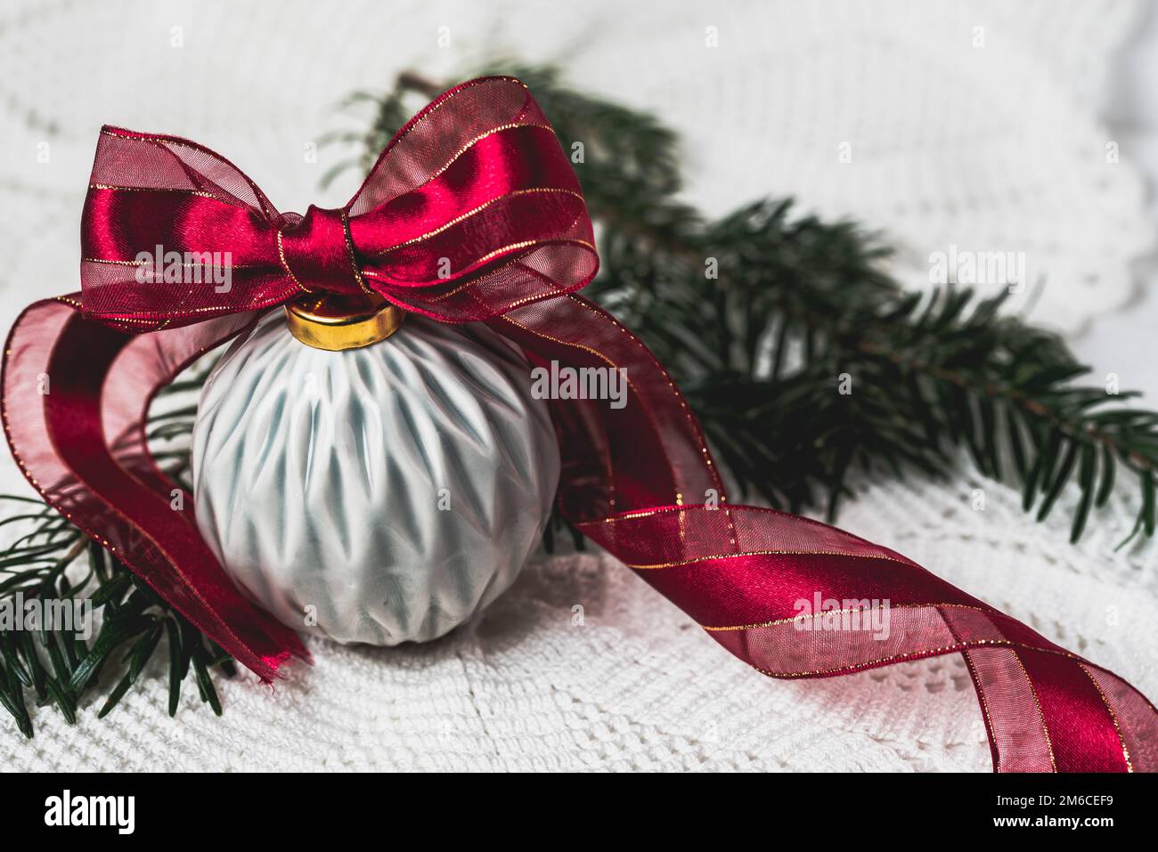 PALLA DI NATALE GRIGIA IN CERAMICA CON NASTRO ROSSO SU UNA TOVAGLIA IN PIZZO Foto Stock