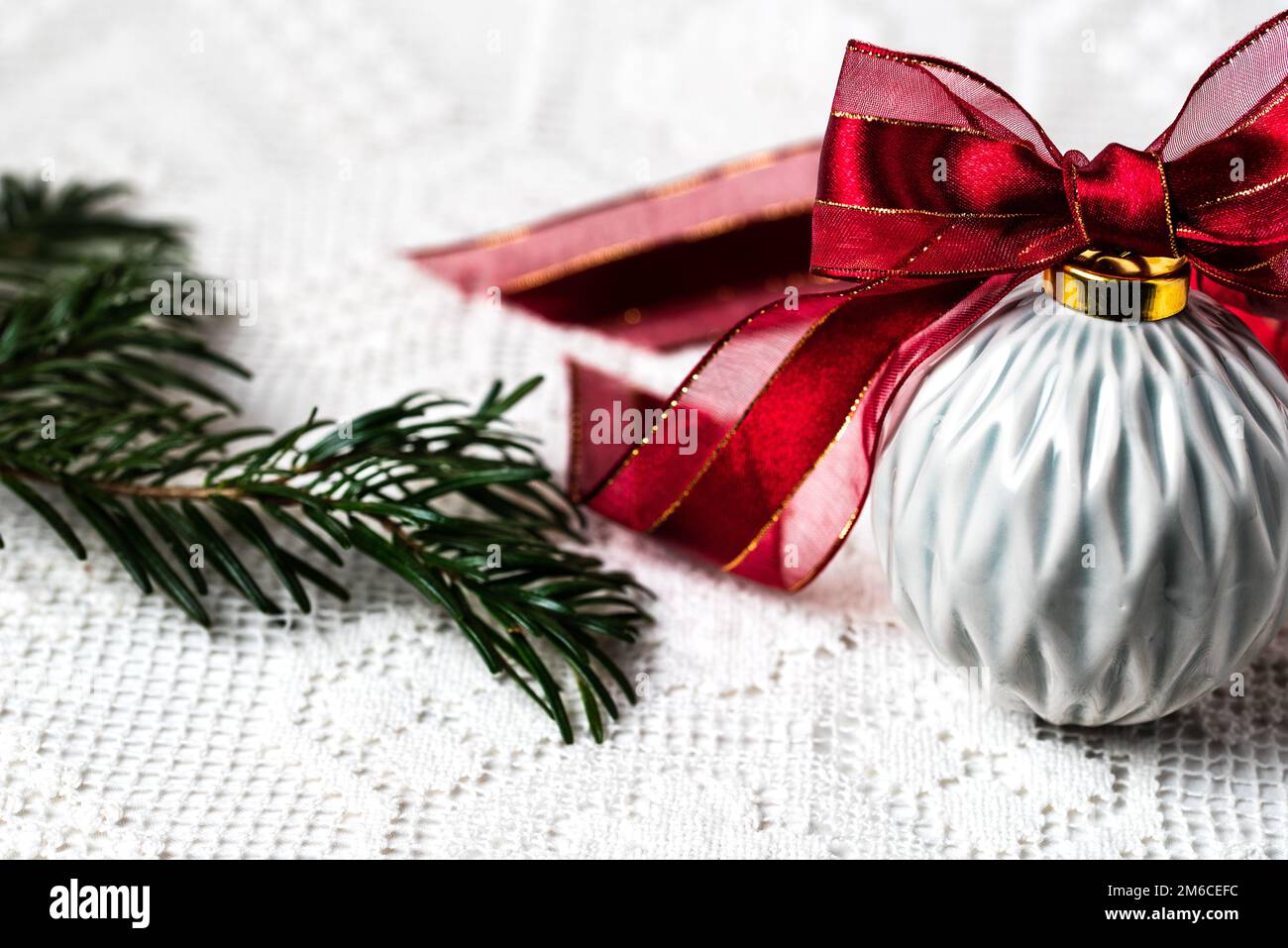 PALLA DI NATALE GRIGIA IN CERAMICA CON NASTRO ROSSO SU UNA TOVAGLIA IN PIZZO Foto Stock