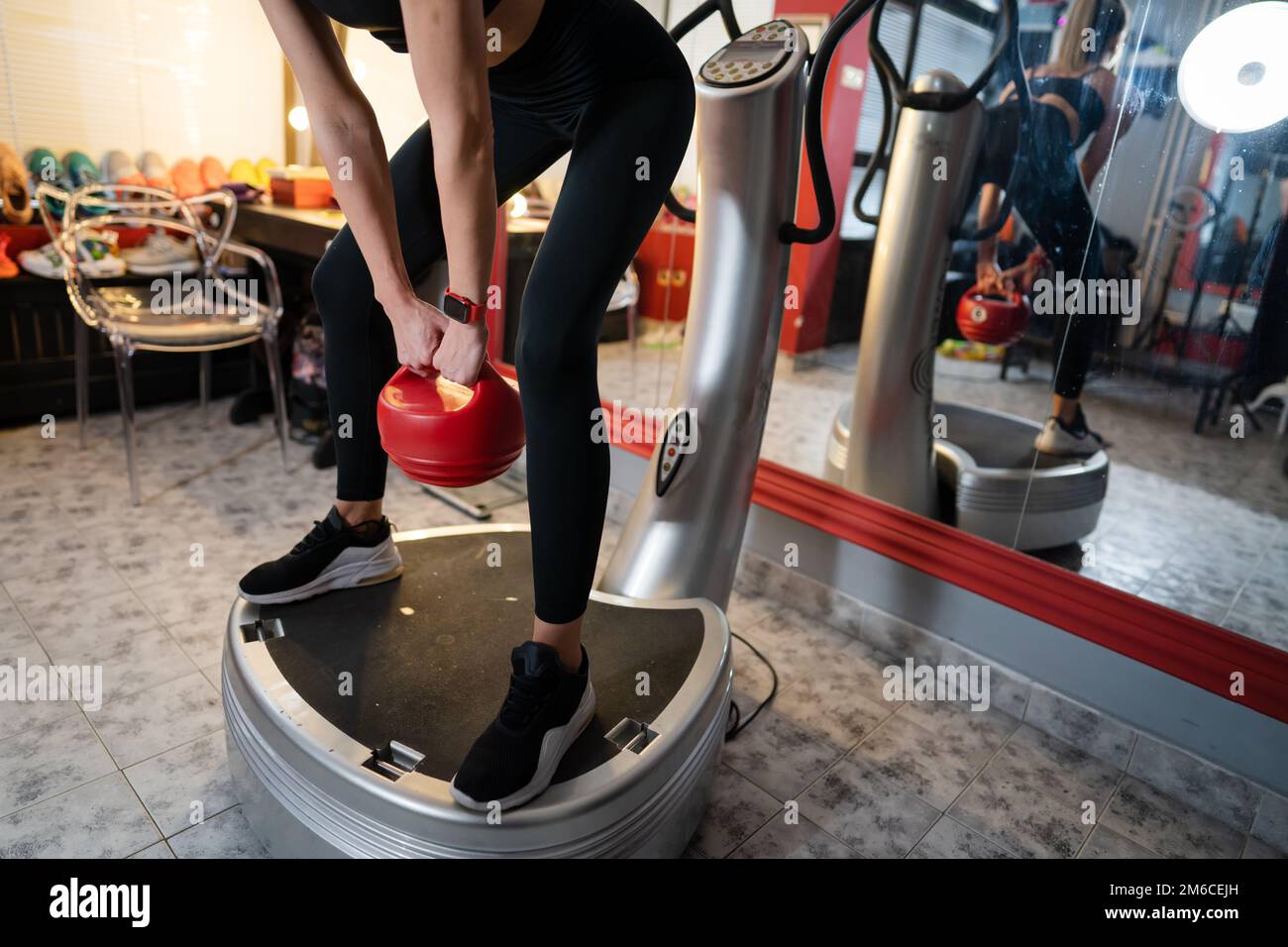 Donna sconosciuta tenere rosso Kettlebell peso mentre in piedi sulla piattaforma di vibrazione della piastra di potenza macchina durante l'allenamento squat esercizio copia spazio Foto Stock