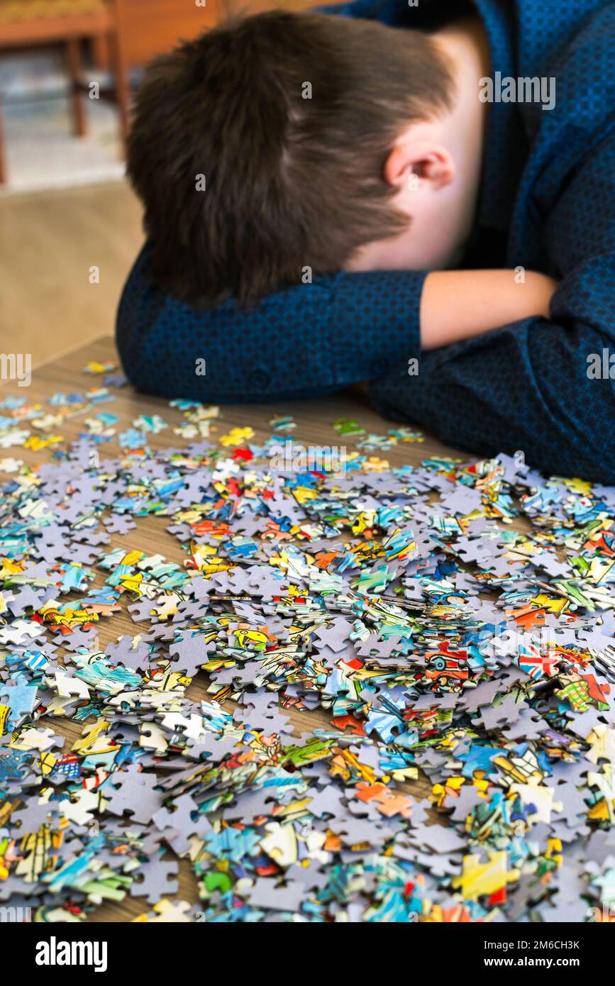 L'adolescente stanco è seduto inclinando la testa accanto a puzzle Foto Stock
