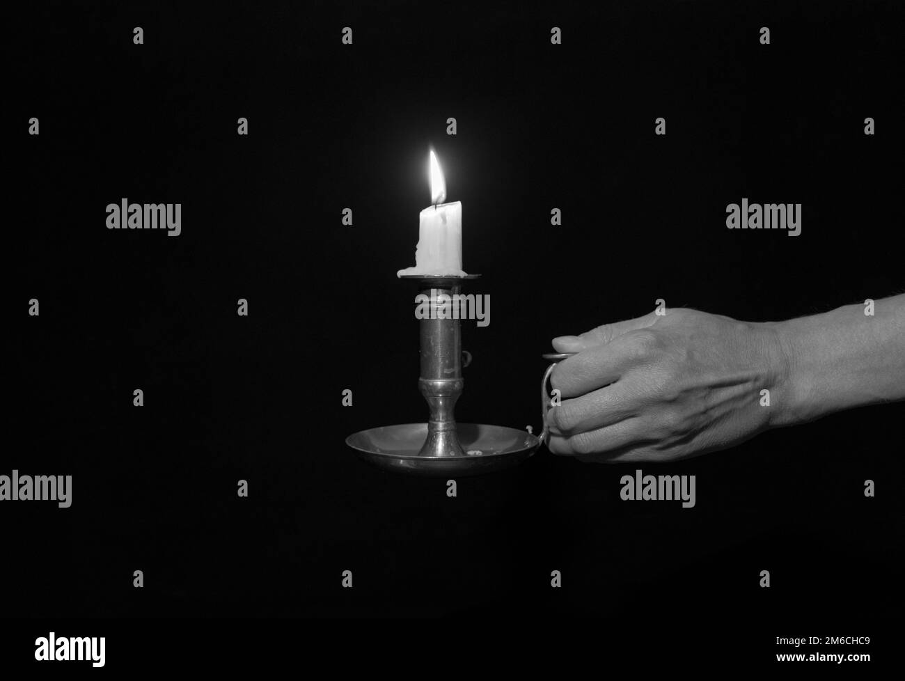 Candelabro decorativo in rame con candele accese in mano femmina su sfondo nero. Bianco e nero Foto Stock