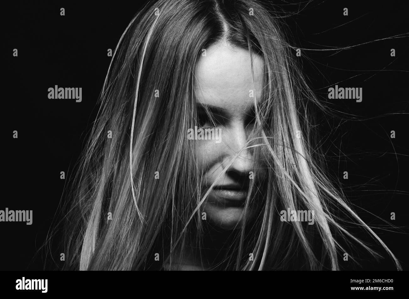 Bella giovane donna tenendo gli occhi chiusi e coprendo il viso con i capelli mentre si trova su sfondo nero Foto Stock