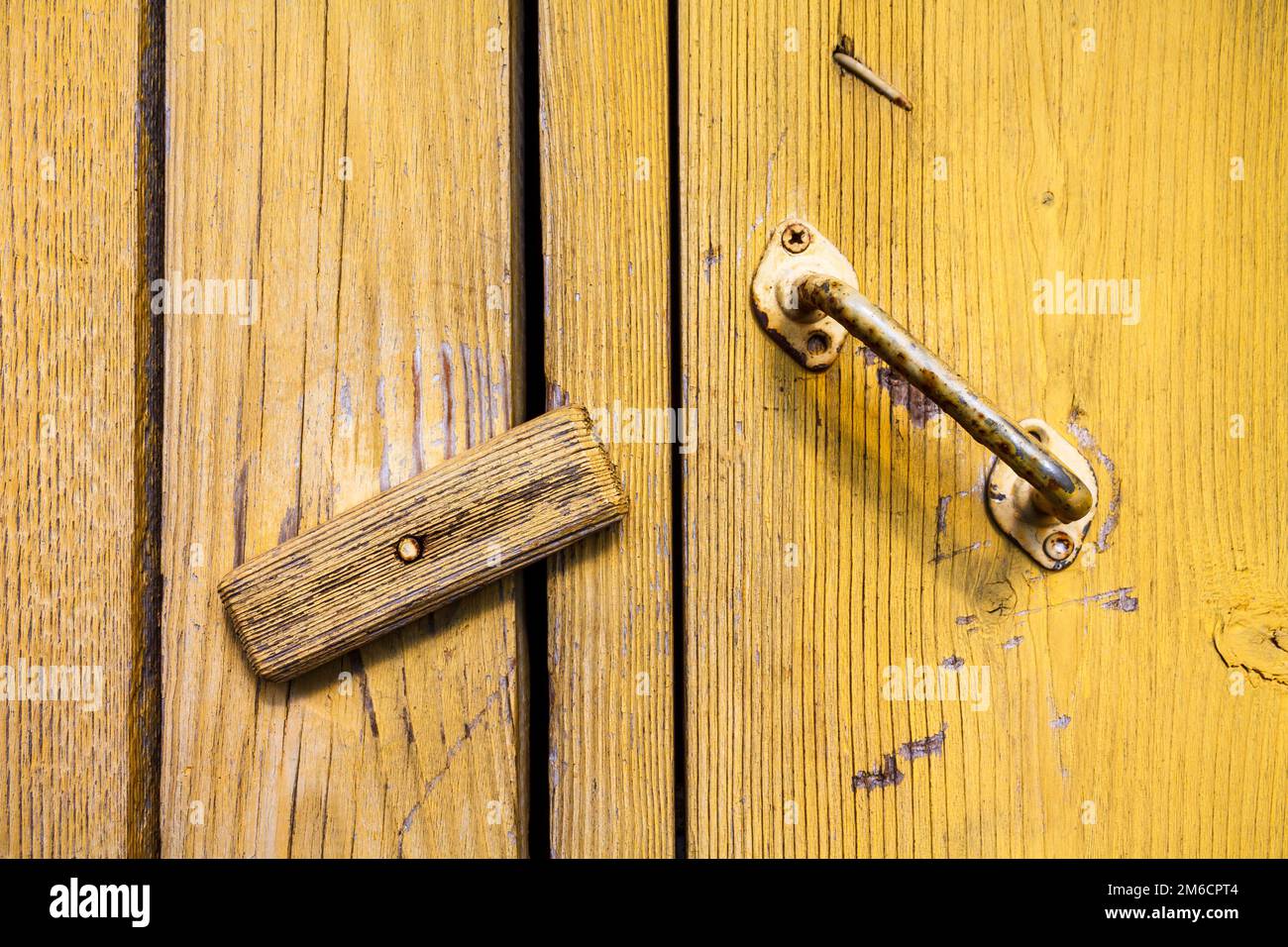 La porta del vecchio villaggio graffiata con una maniglia arrugginita dipinta di vernice gialla è chiusa su una serratura di legno. Foto Stock