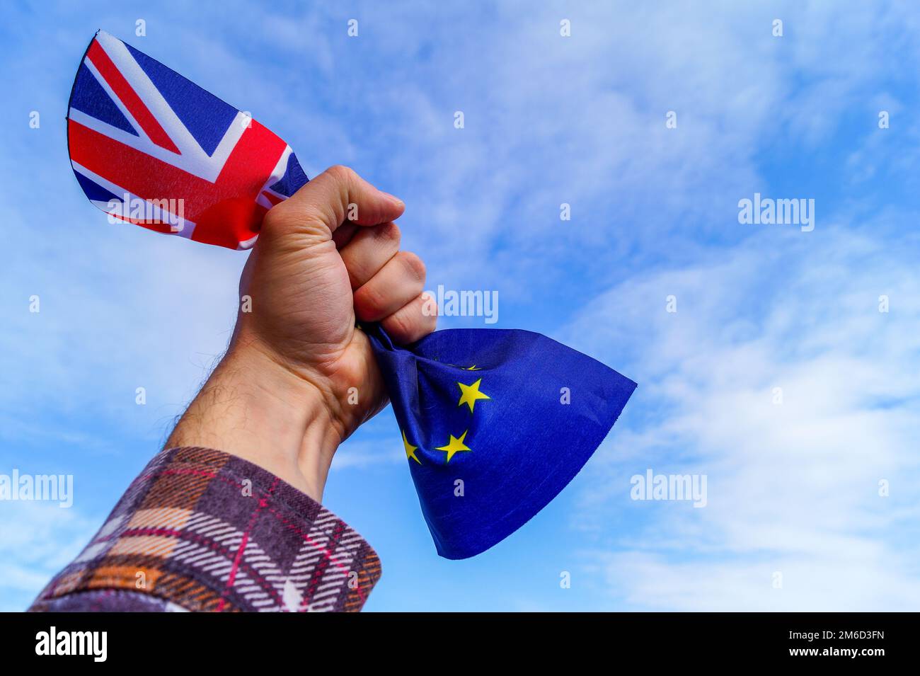 Una mano maschile tiene in pugno le bandiere dell’Inghilterra e dell’Unione europea contro un cielo blu e simboleggia la Brexit o la No Brexit. Foto Stock