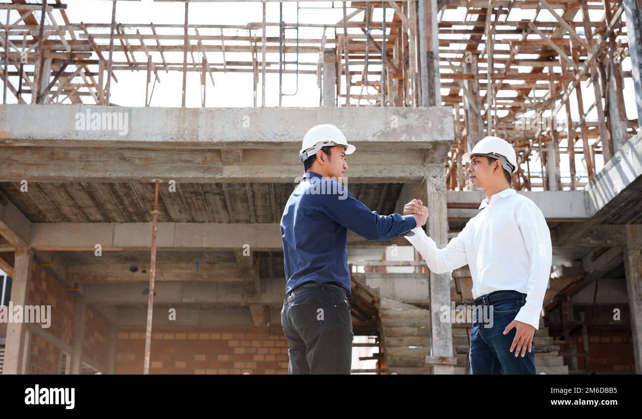 Gli ingegneri di architetti e operai edili scuotono le mani mentre lavorano in cantiere all'aperto. Foto Stock