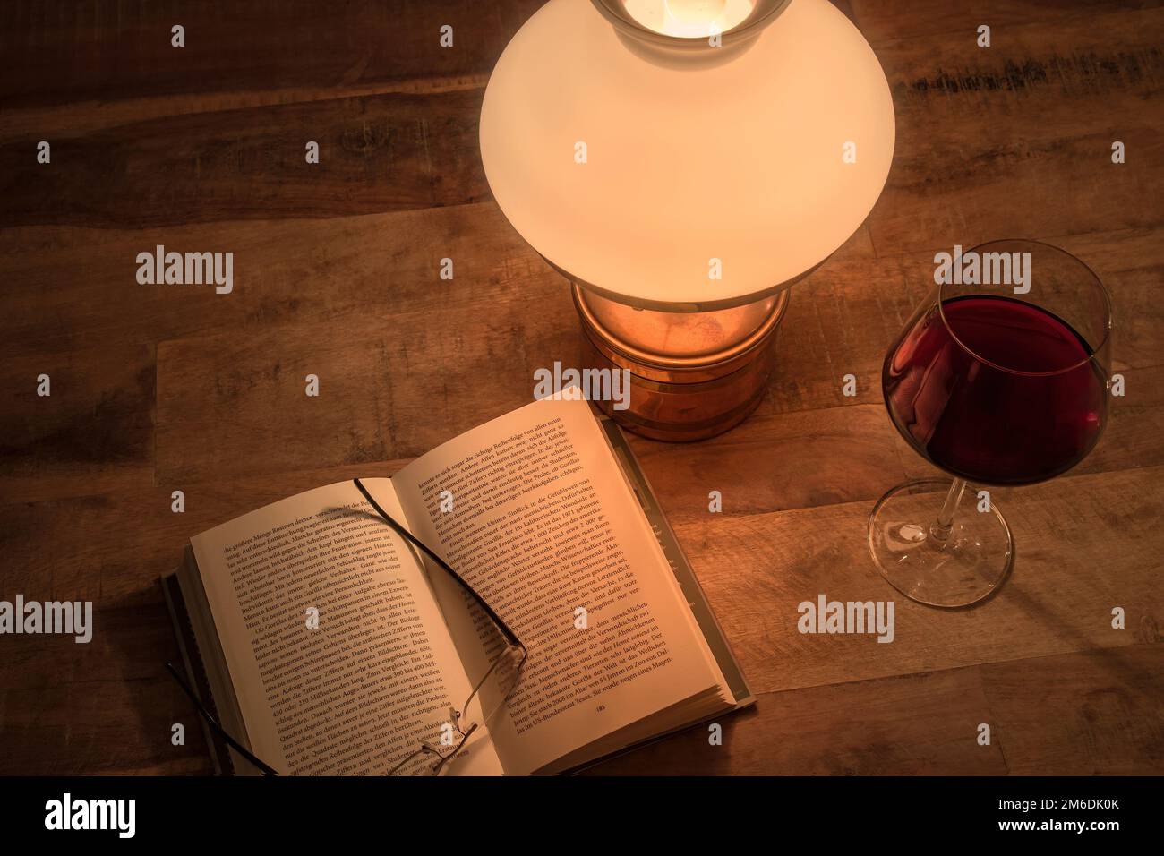 Apri libro vecchio olio lampada e bicchiere di vino rosso su tavolo di legno Foto Stock