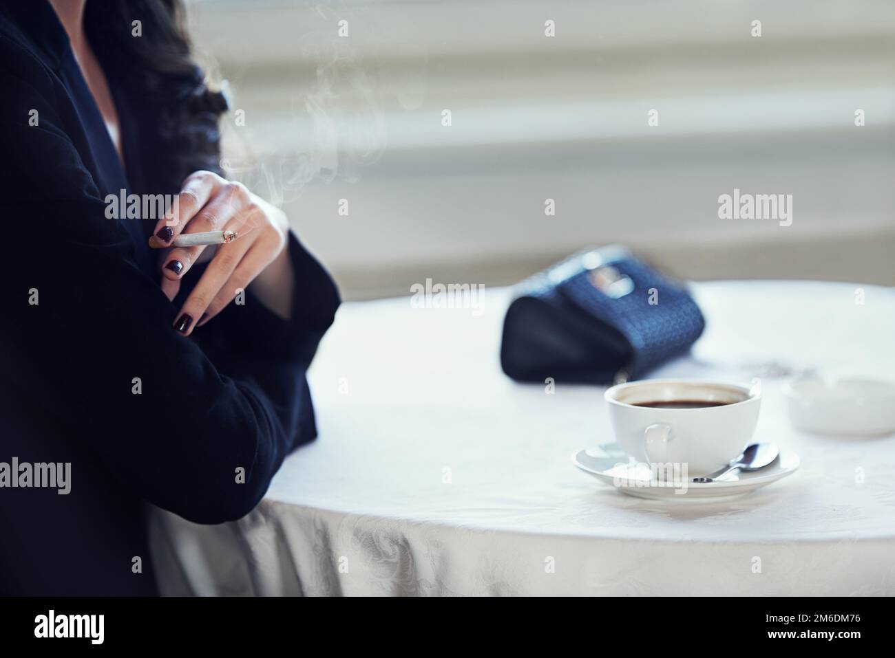 Accessori classici di ricchezza e stile. una donna elegante seduta a un tavolo che fuma con una tazza di caffè davanti a lei. Foto Stock