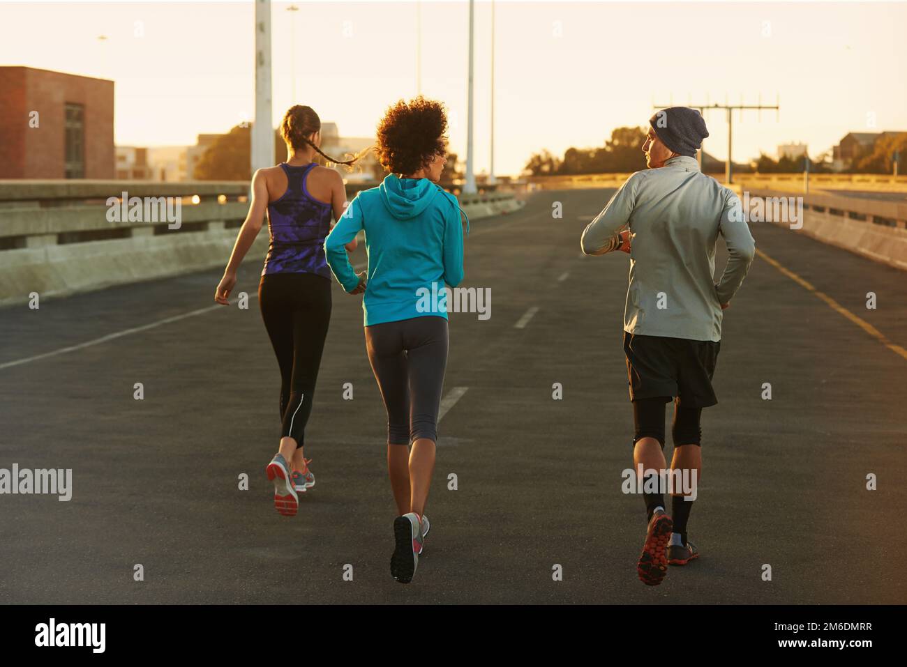 Correre in una città tranquilla. Ripresa da dietro di tre giovani joggers che corrono lungo una strada vuota all'alba. Foto Stock