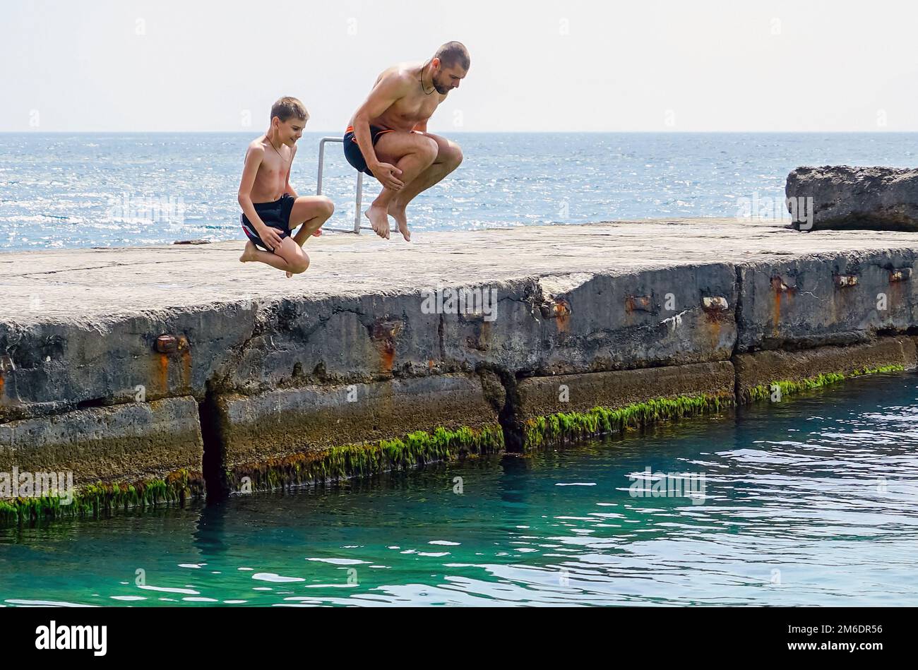 Padre e figlio si tuffano in mare dal molo . Foto Stock