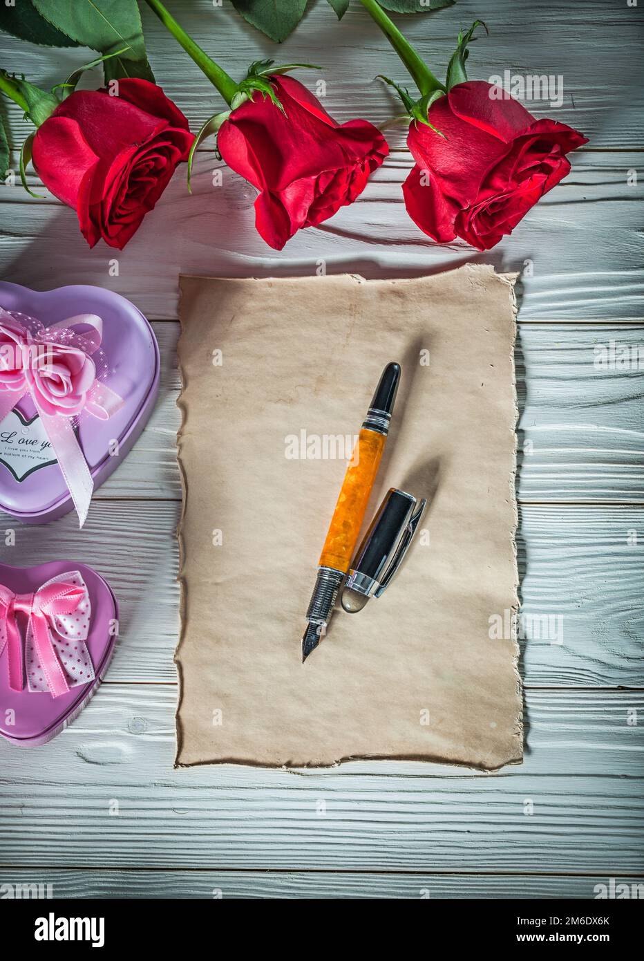 Metallo a forma di cuore scatole presenti rose rosse vintage foglio penna fontana su legno bordo vacanze concetto. Foto Stock