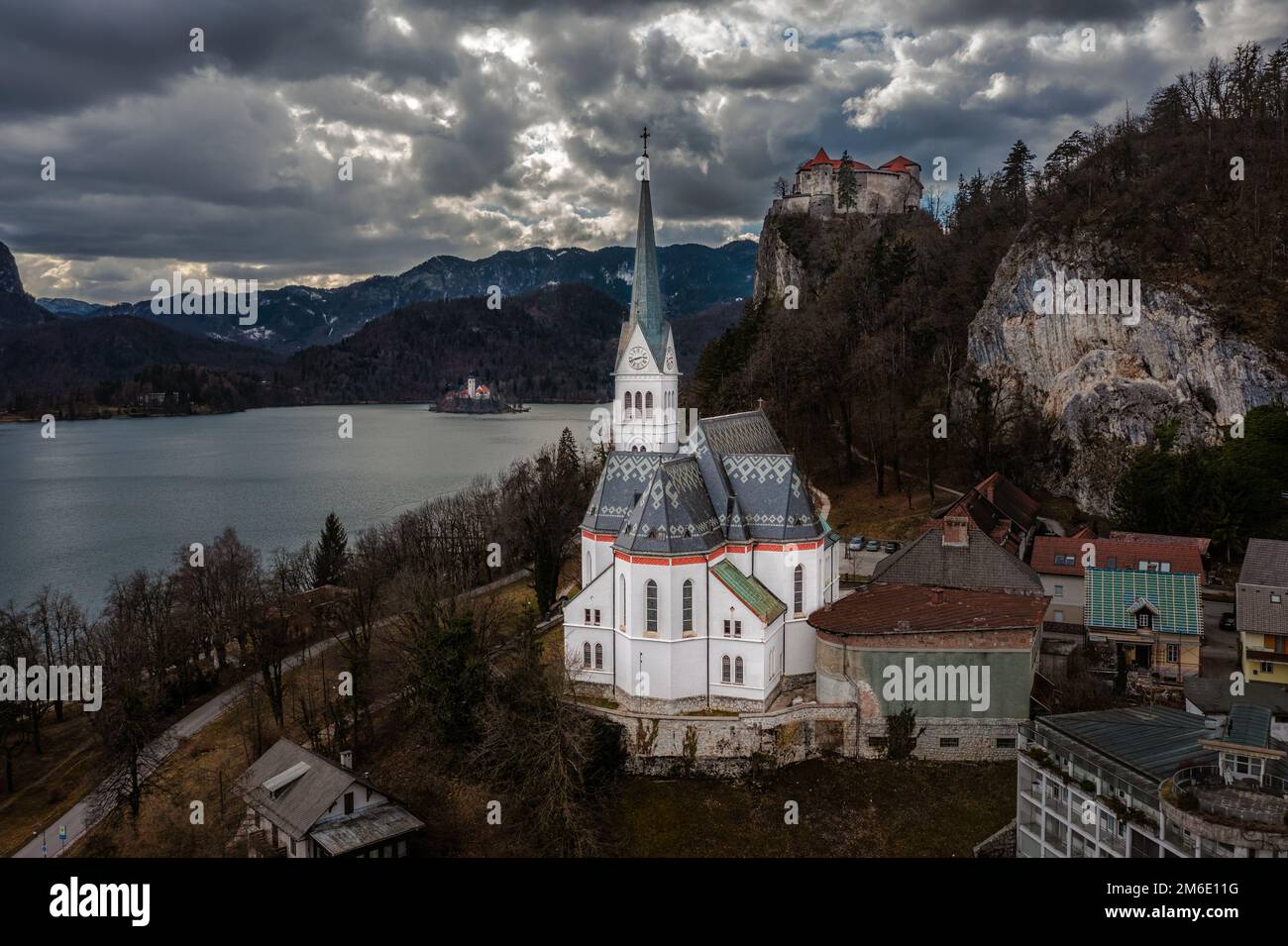 Bled, Slovenia - veduta aerea di San Chiesa Parrocchiale di Martin con il castello di Bled (Blejski Grad), l'isola di Bled e le Alpi Giulie sullo sfondo su un nuvoloso Foto Stock