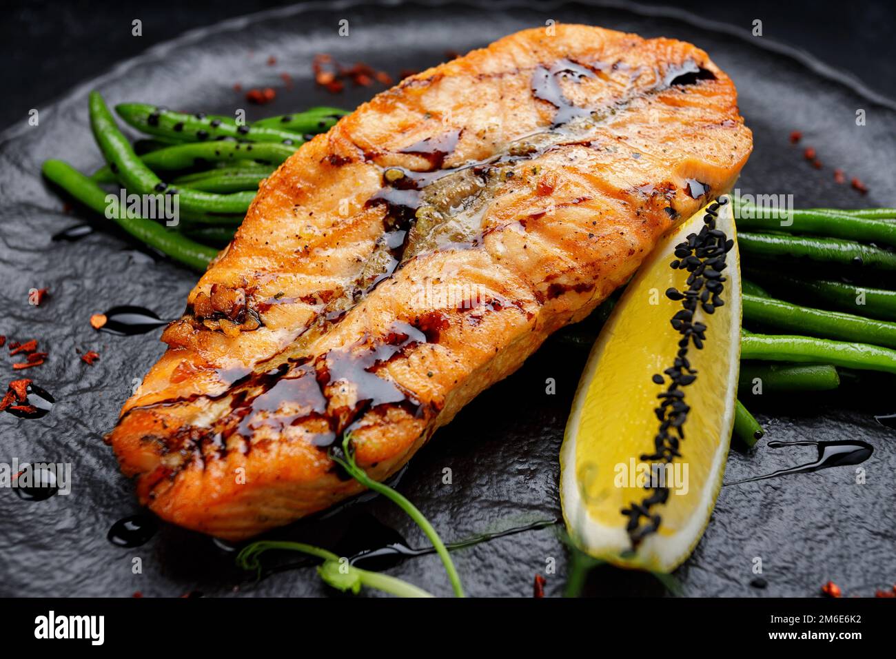 Bistecca di salmone alla griglia con asparagi e limone su un piatto nero Foto Stock
