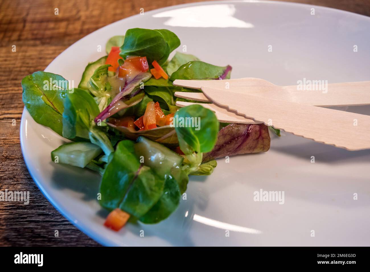Posate di legno ecocompatibili su un piatto con insalata laterale. Alternativa alla plastica monouso meno ecologica in un bar. Foto Stock