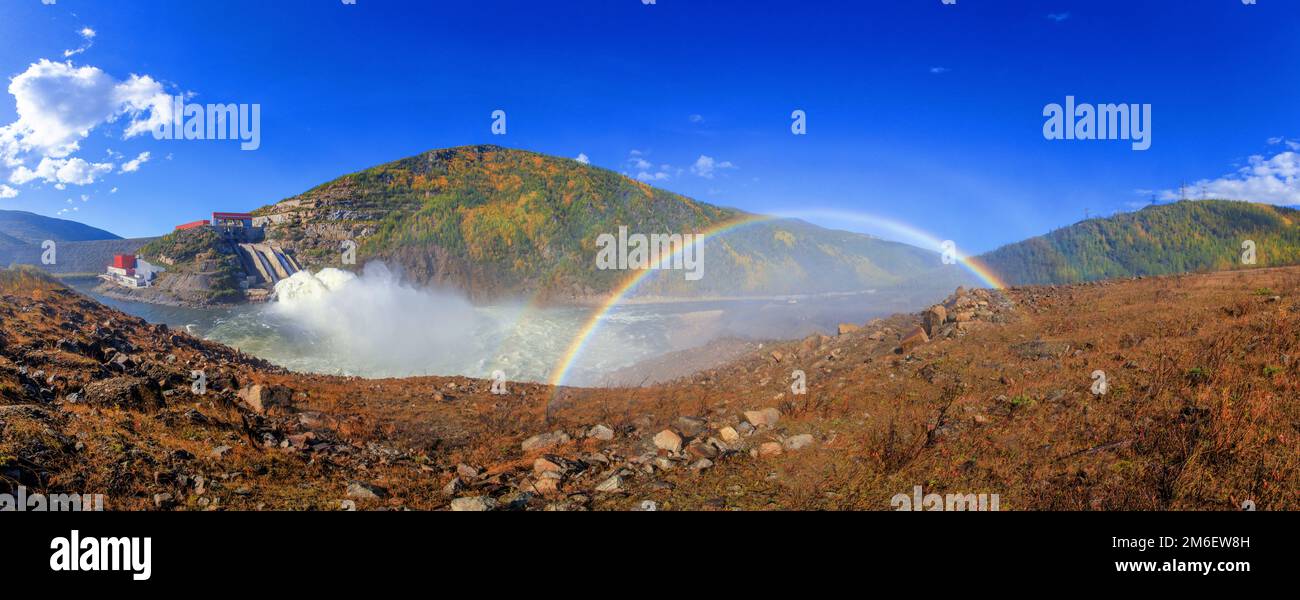 Un bellissimo arcobaleno luminoso a grandezza naturale sullo sfondo delle colline autunnali e un piccolo ruscello. Arcobaleno sulla idroelettricità d Foto Stock