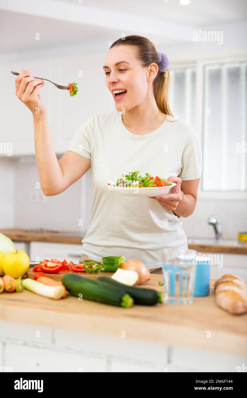 Ritratto di donna in piedi in casa cucina e degustazione insalata di verdure Foto Stock