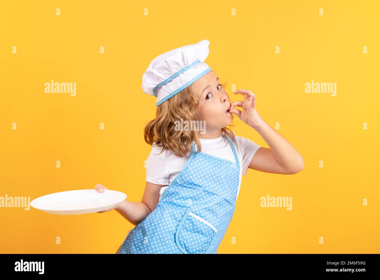 Divertente cuoco del capretto con il piatto della cucina, ritratto dello studio. Cucina, cucina e bambini. Bambino in cappello e grembiule chef su sfondo isolato studio. Foto Stock