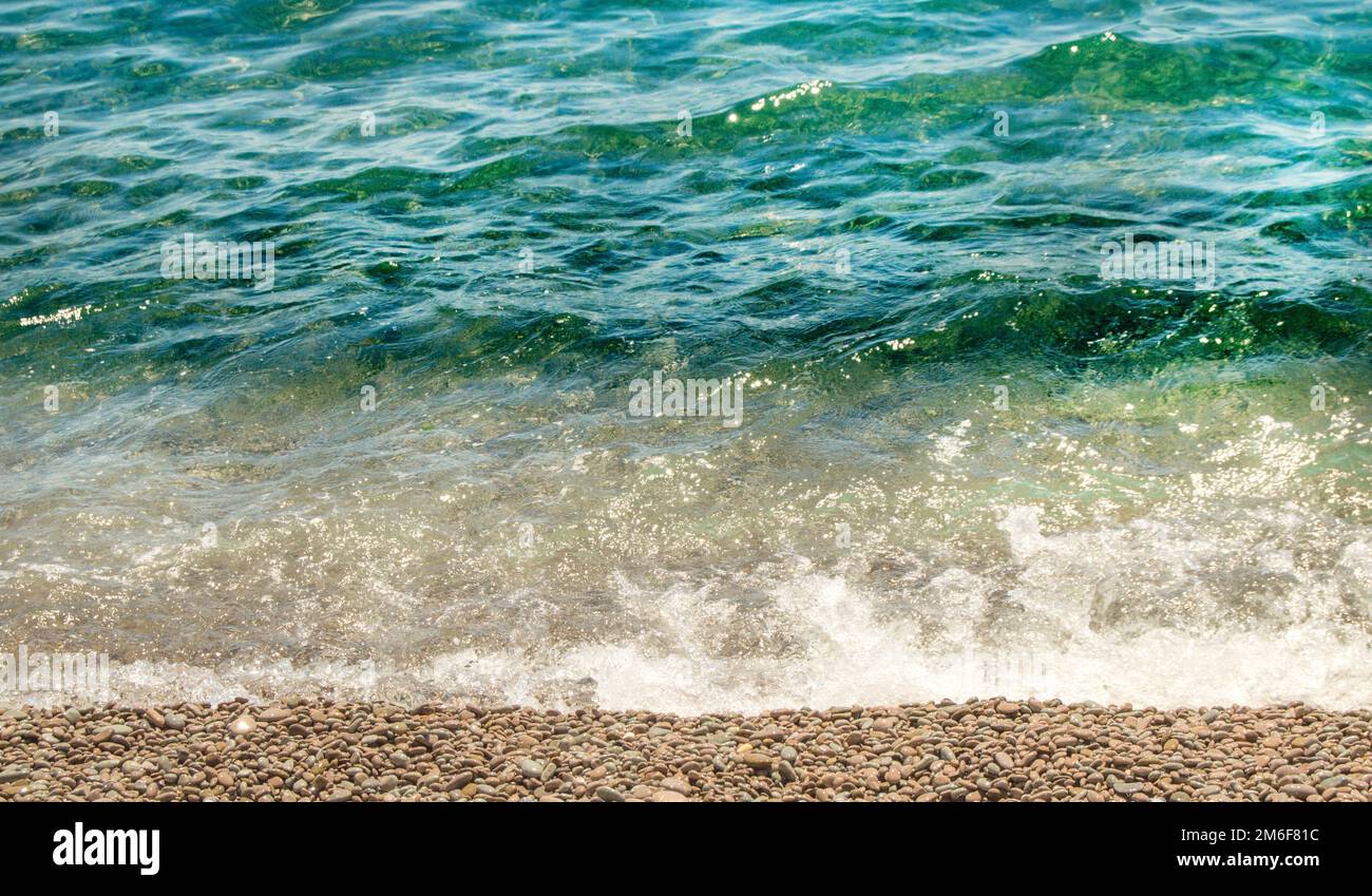 Vista ravvicinata della costa marina con acqua turchese e una spiaggia di ciottoli in una giornata estiva soleggiata, mare calmo, viaggi e vacanze Foto Stock