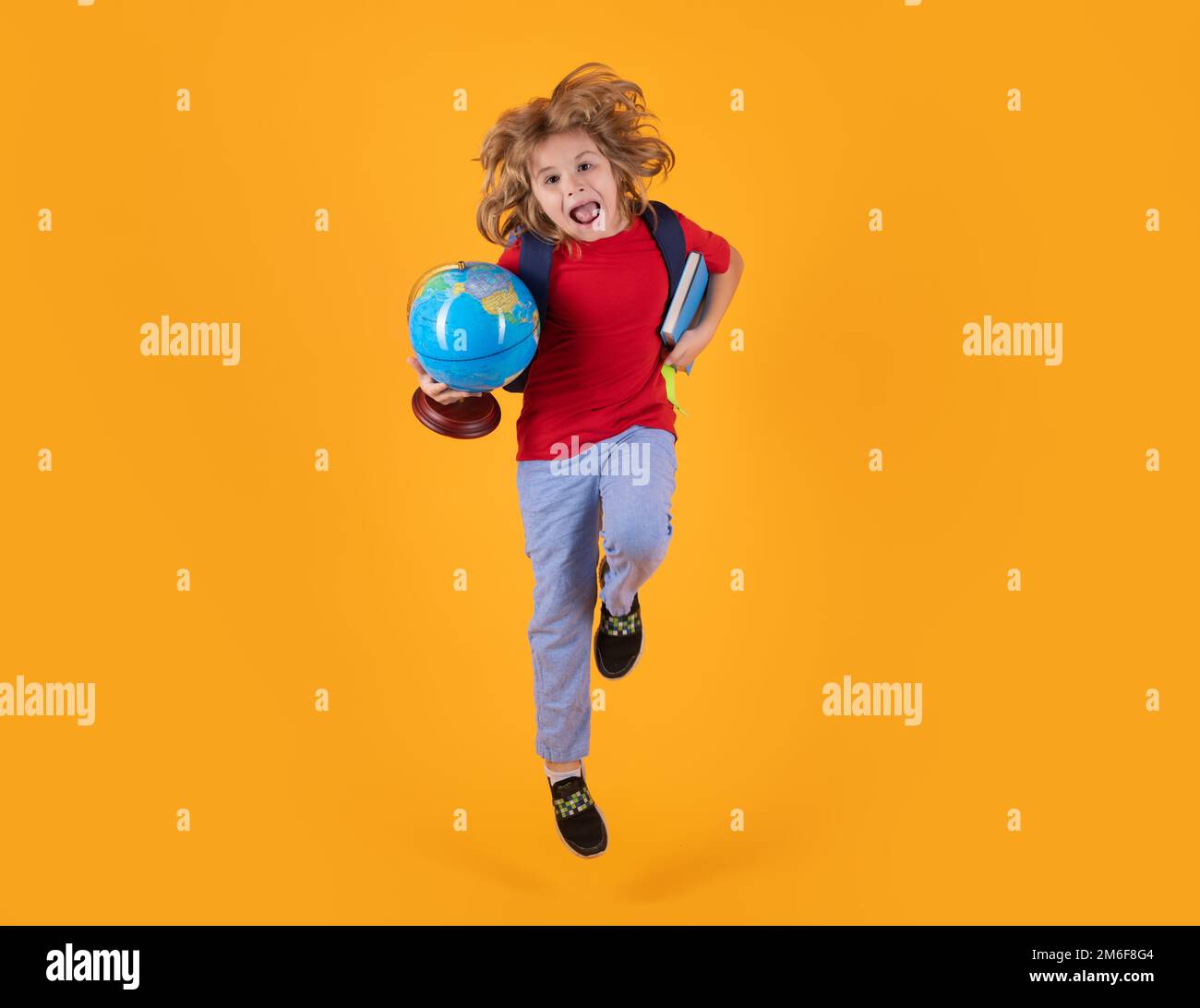 Ritorno a scuola. Corpo completo di bambino ragazzo scuola elementare in abiti casual con backpackand libro globo saltando su sfondo blu. Foto Stock