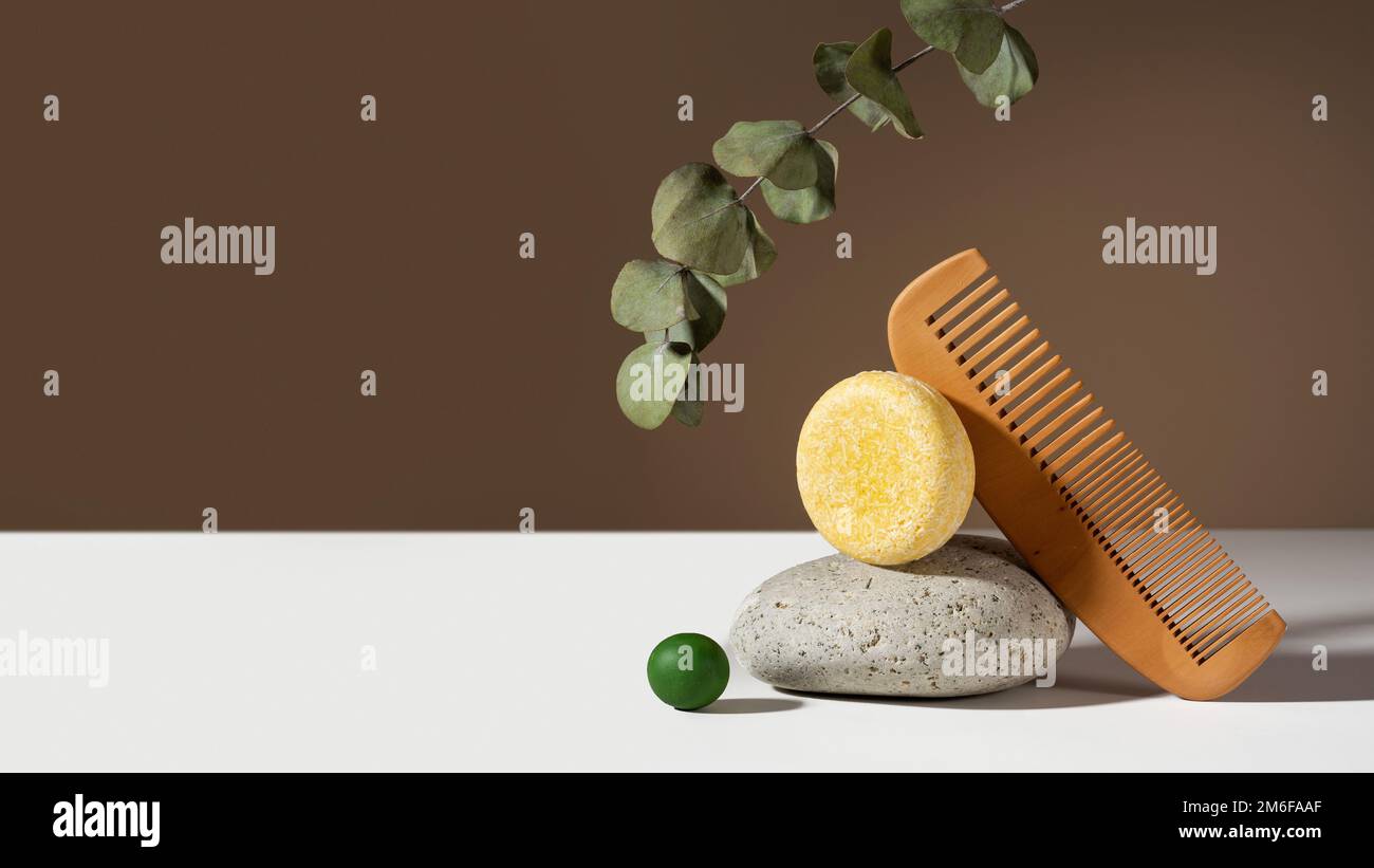 Moderna composizione geometrica di una solida barra di shampoo. eucalipto, pietra e legno pettini equilibrati su fondo marrone. Concept senza plastica Foto Stock