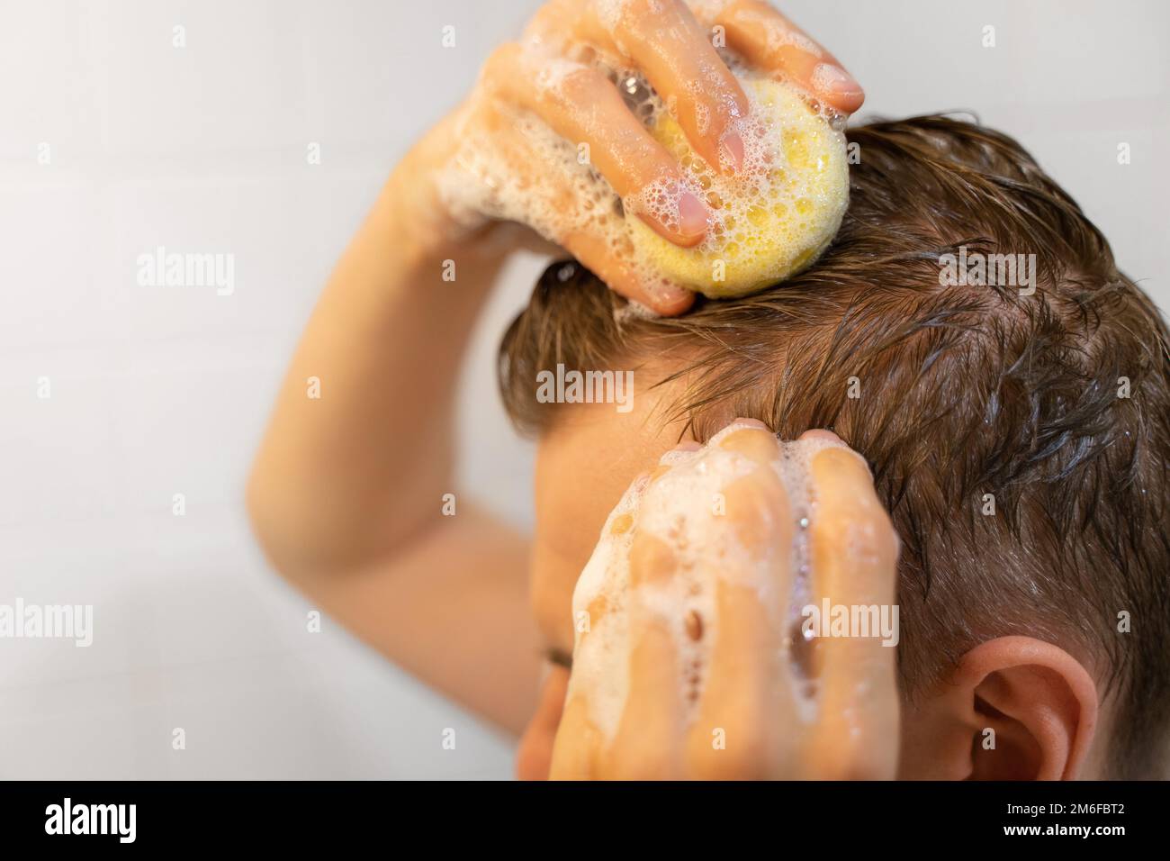 Un uomo usa un solido shampoo bar in bagno. Cura sostenibile dei capelli. Uno shampoo applicato al cuoio capelluto. Senza plastica, senza sprechi, acqua bassa Foto Stock