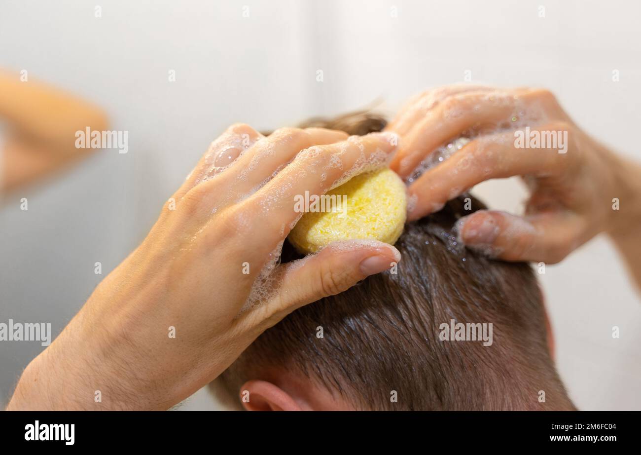 Un uomo applica una barra solida dello shampoo ai capelli. Cura sostenibile dei capelli. Uomo in bagno. Senza plastica, senza sprechi, ingredienti a basso contenuto di acqua. Foto Stock