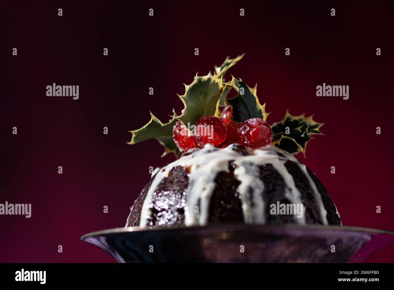 Tradizionale dessert natalizio al budino di frutta, decorato con ciliegie e foglie, con un classico sfondo rosso, blu e viola Foto Stock