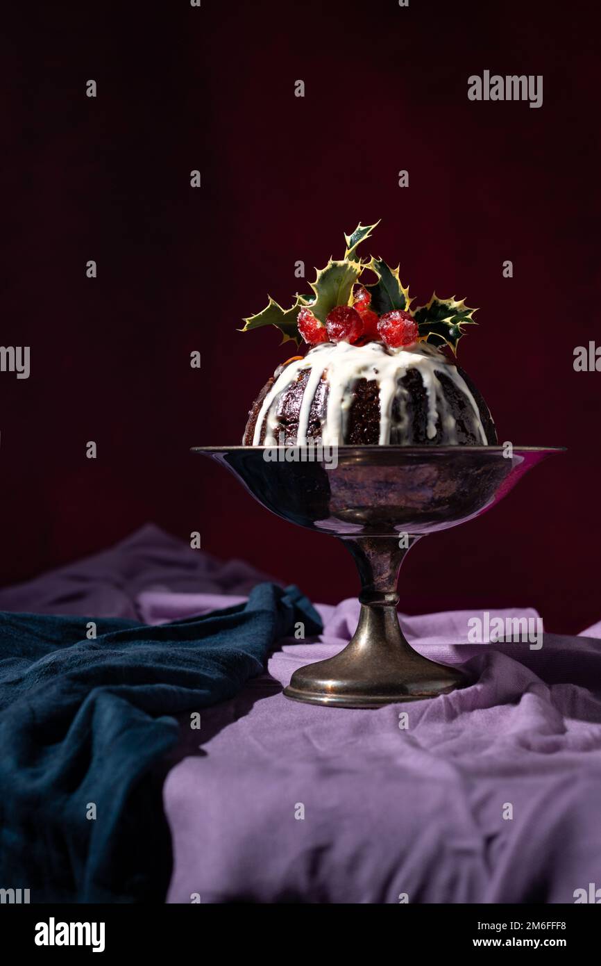 Tradizionale dessert natalizio al budino di frutta, decorato con ciliegie e foglie, con un classico sfondo rosso, blu e viola Foto Stock