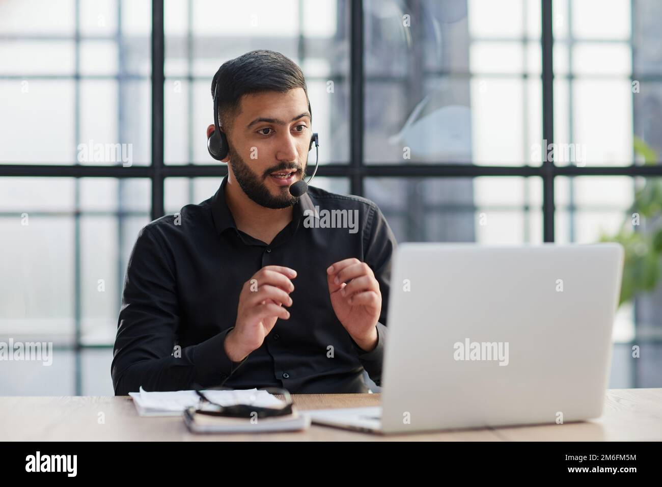 Un giovane e bell'operatore telefonico di assistenza clienti di sesso maschile con cuffie che lavorano in ufficio. Foto Stock