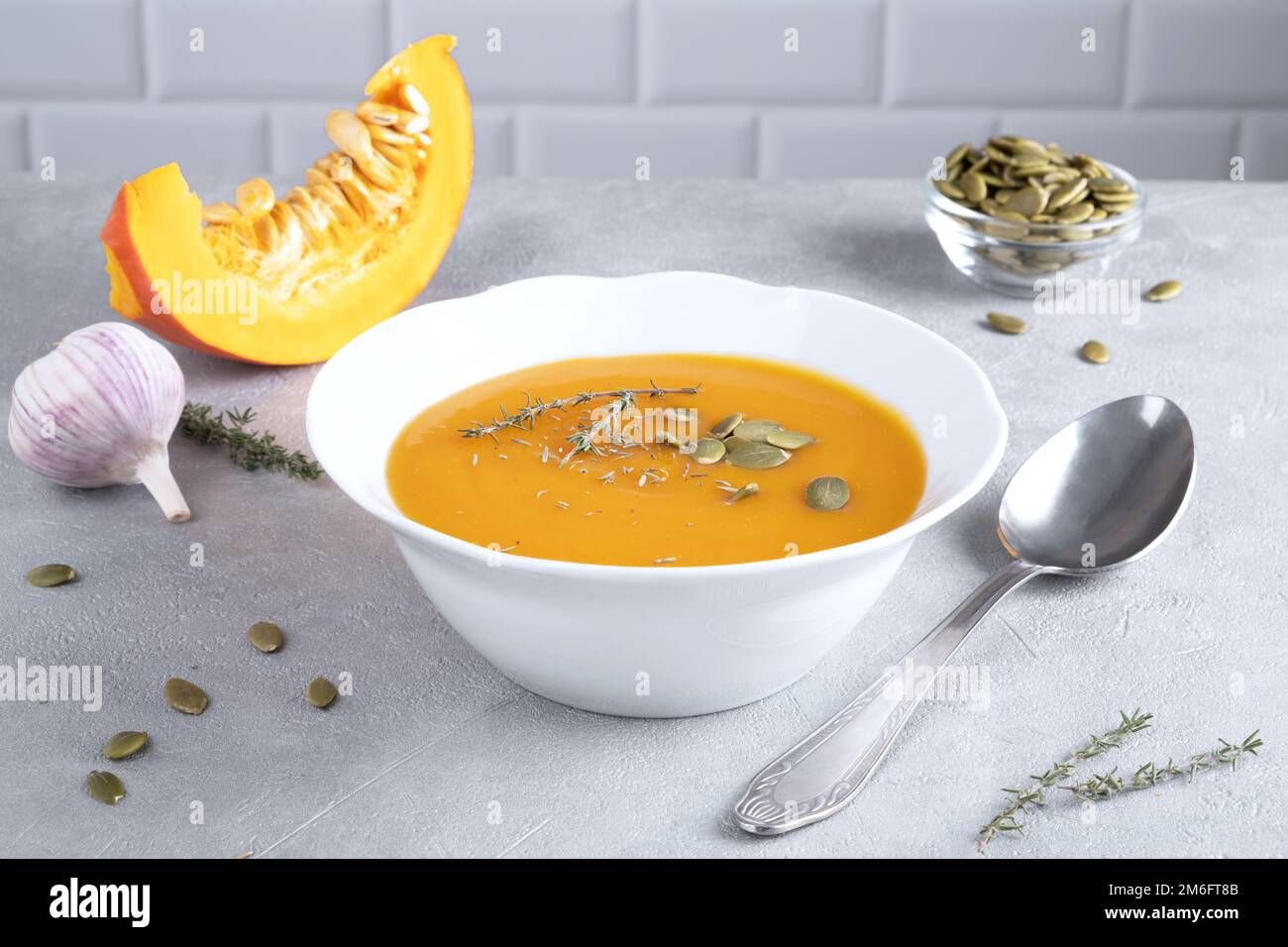 Zuppa di purea di zucca con semi di zucca e timo in un piatto bianco e un pezzo di zucca matura. Dieta sana. Messa a fuoco selettiva. Foto Stock