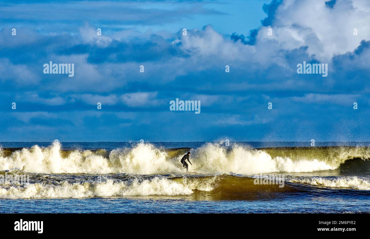 Lossiemouth East Beach Moray costa Scozia solista surfista e onde infrangenti in inverno Foto Stock