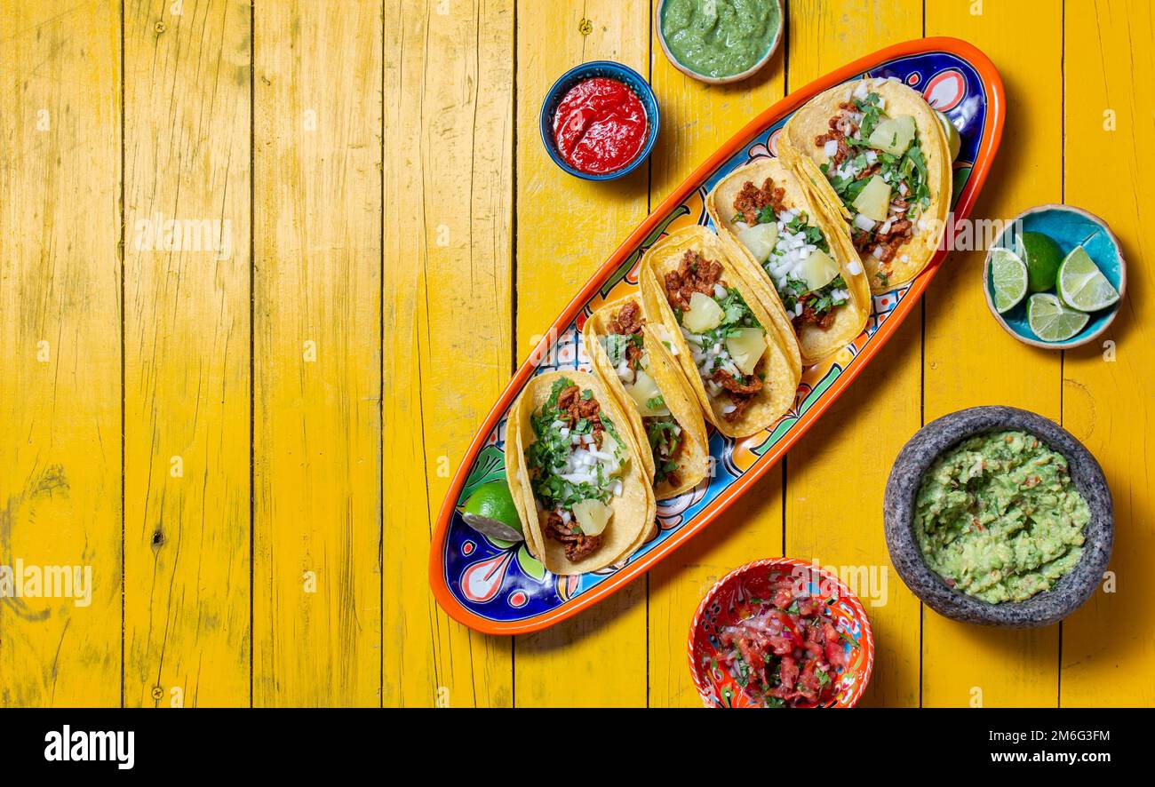 Sfondo messicano con tacos al pastor e salse messicane. Sfondo di legno giallo, spazio copia, vista dall'alto. Foto Stock