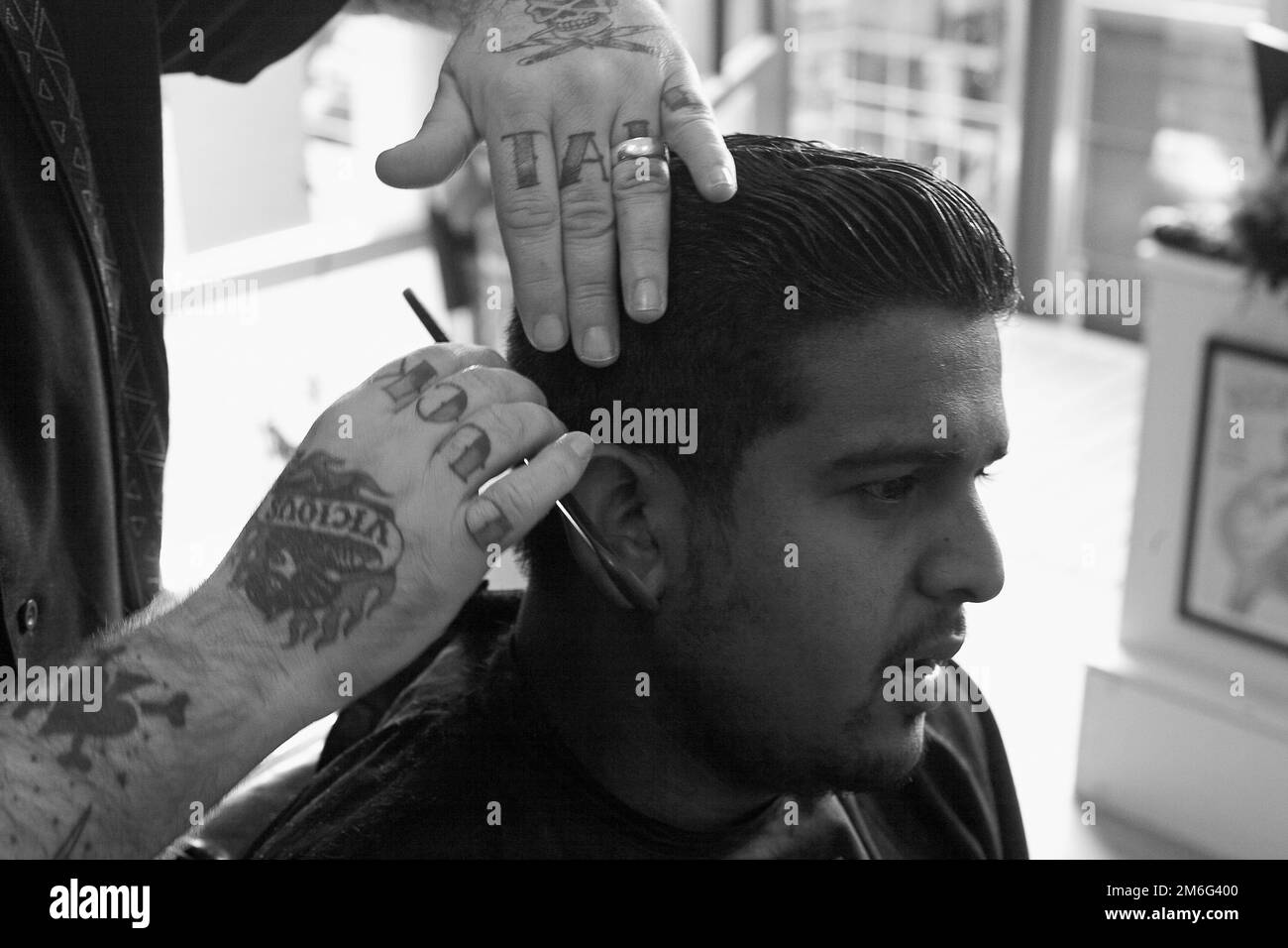 Barber sta tagliando i capelli del giovane uomo. Vista laterale dell'uomo che ottiene la rifinitura corta dei capelli al barbiere con le forbici Foto Stock