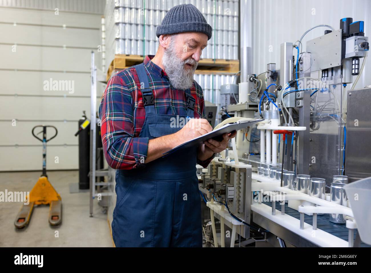 Lavoratore di fabbrica che controlla il processo di inscatolamento della birra Foto Stock