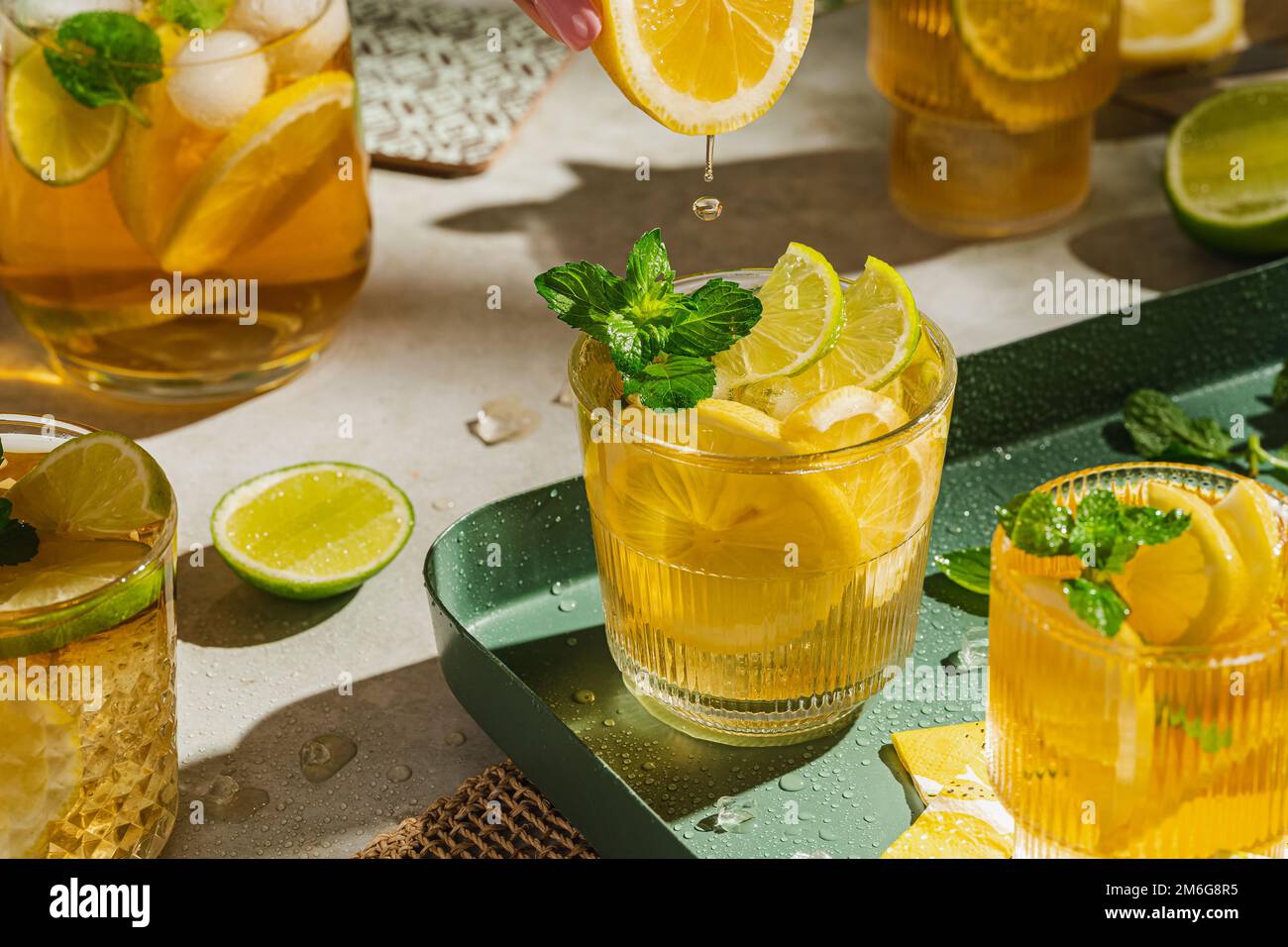 Tradizionale tè freddo fatto in casa con limone, menta e ghiaccio in bicchieri. Bevanda fredda estiva su sfondo verde. Concetto di sano cibo estivo. Messa a fuoco selettiva Foto Stock