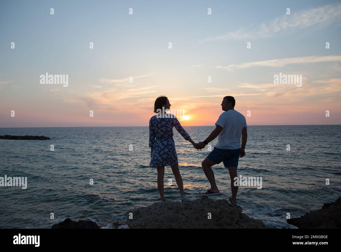 uomo e donna, lui e lei in piena crescita, silhouette di coppia innamorata contro sfondo di mare e tramonto stanno tenendo le mani. godimento del momento, t Foto Stock