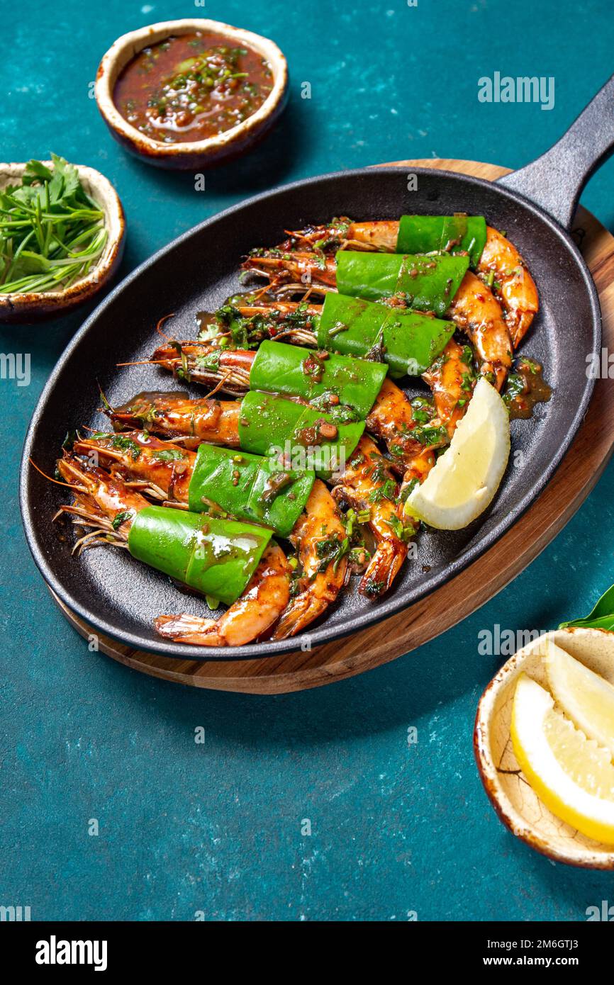 Gamberi piccanti di tigre d'aglio Sgamberetti in padella con foglie di limone su terra di forno blu, primo piano. Foto Stock