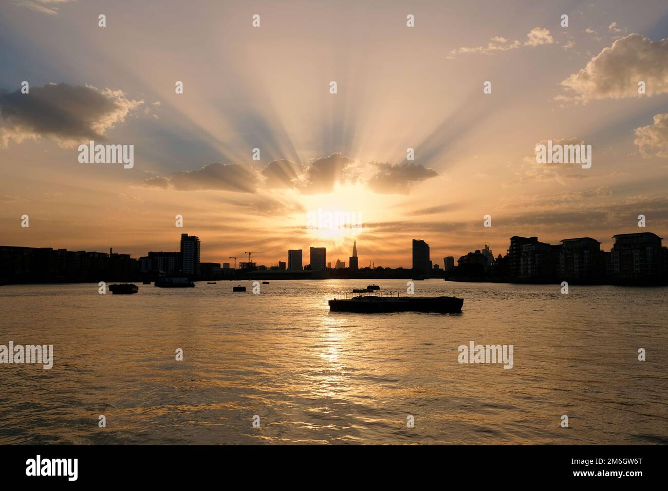I raggi dorati del sole splendono da dietro lo Shard in lontananza sul tamigi al tramonto a Londra Foto Stock