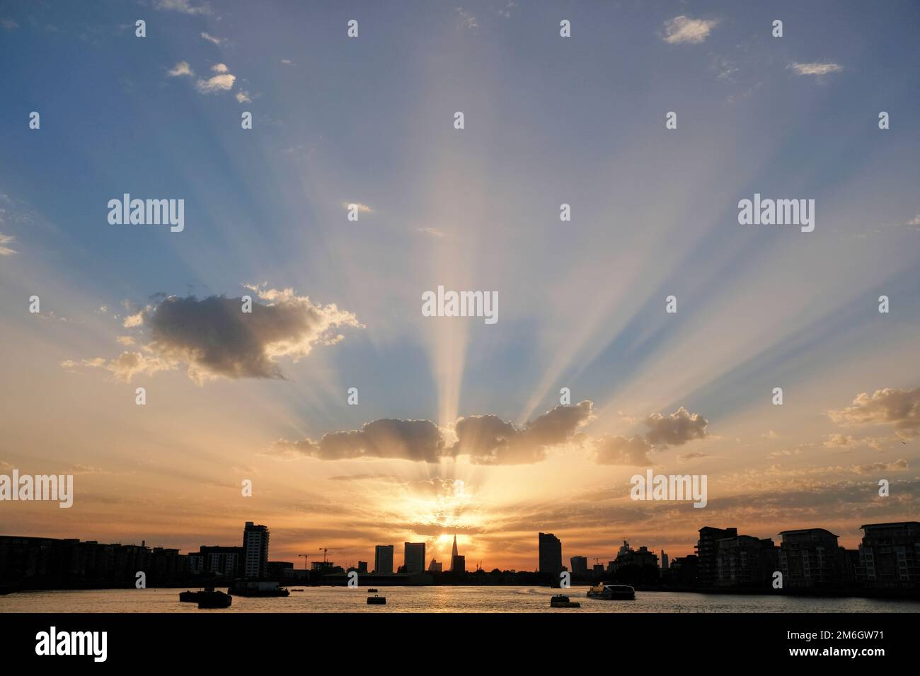 I raggi dorati del sole splendono da dietro lo Shard in lontananza sul tamigi al tramonto a Londra Foto Stock