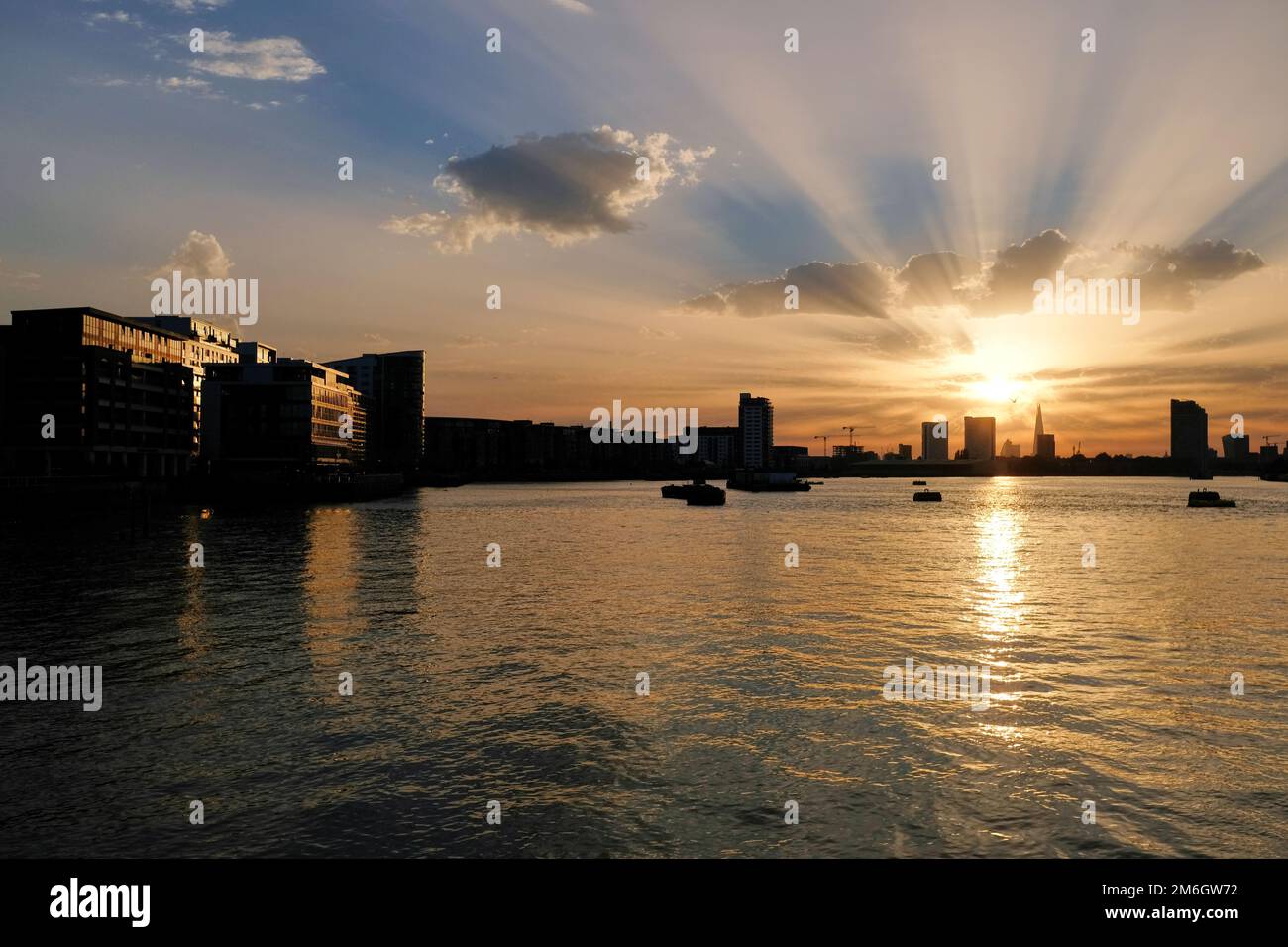 I raggi dorati del sole splendono da dietro lo Shard in lontananza sul tamigi al tramonto a Londra Foto Stock