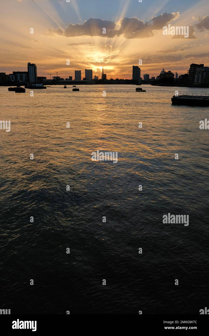 I raggi dorati del sole splendono da dietro lo Shard in lontananza sul tamigi al tramonto a Londra Foto Stock