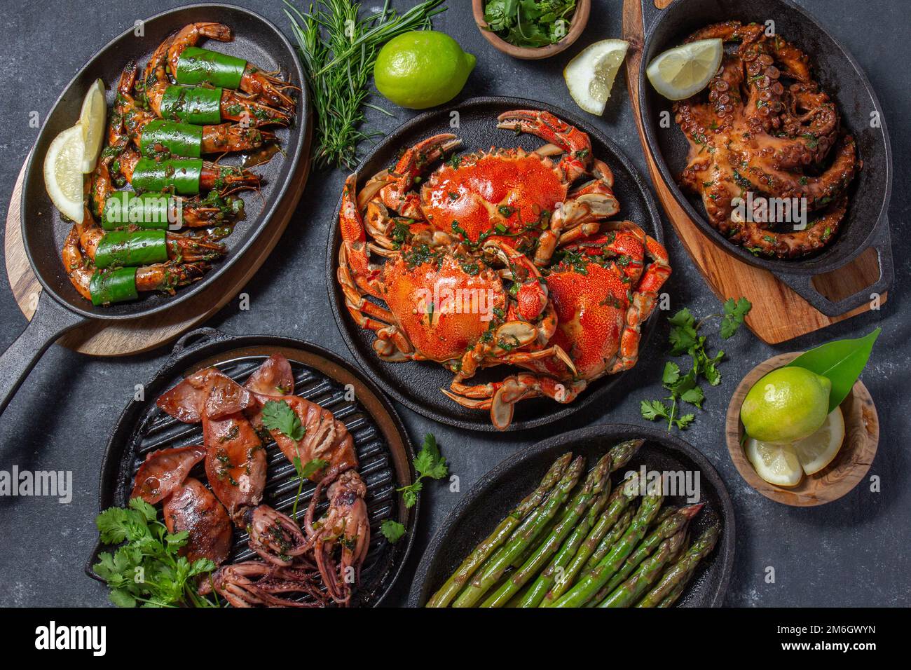 Set di piatti di pesce. Granchi, polpi, calamari e gamberetti sulle teglie e piatti di ghisa su fondo nero. Vista dall'alto Foto Stock