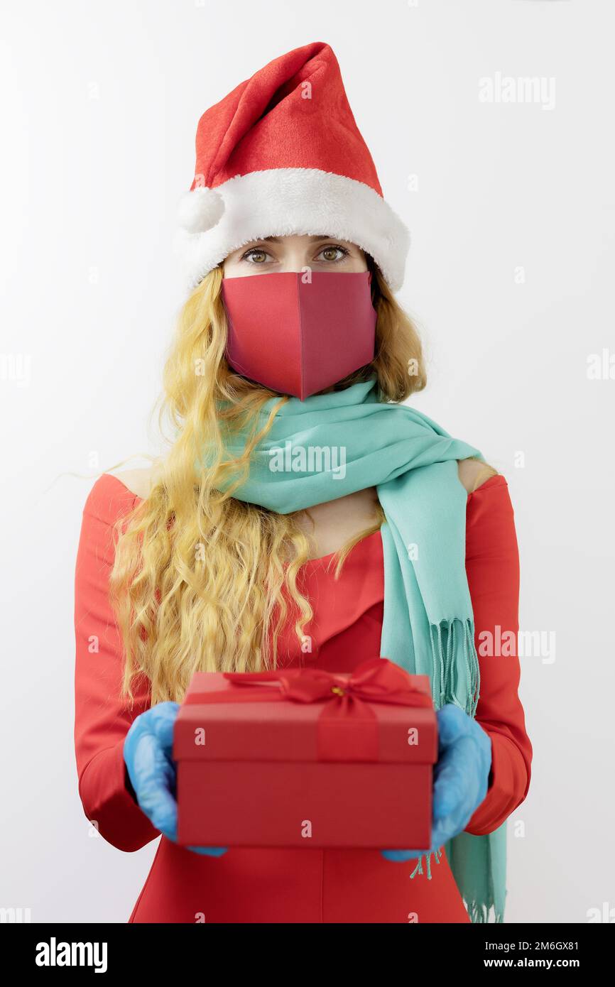Lady Babbo Natale in una maschera protettiva e guanti contiene una scatola con un regalo. Regalo sterile. Natale protetto. Fuoco sul volto della ragazza Foto Stock