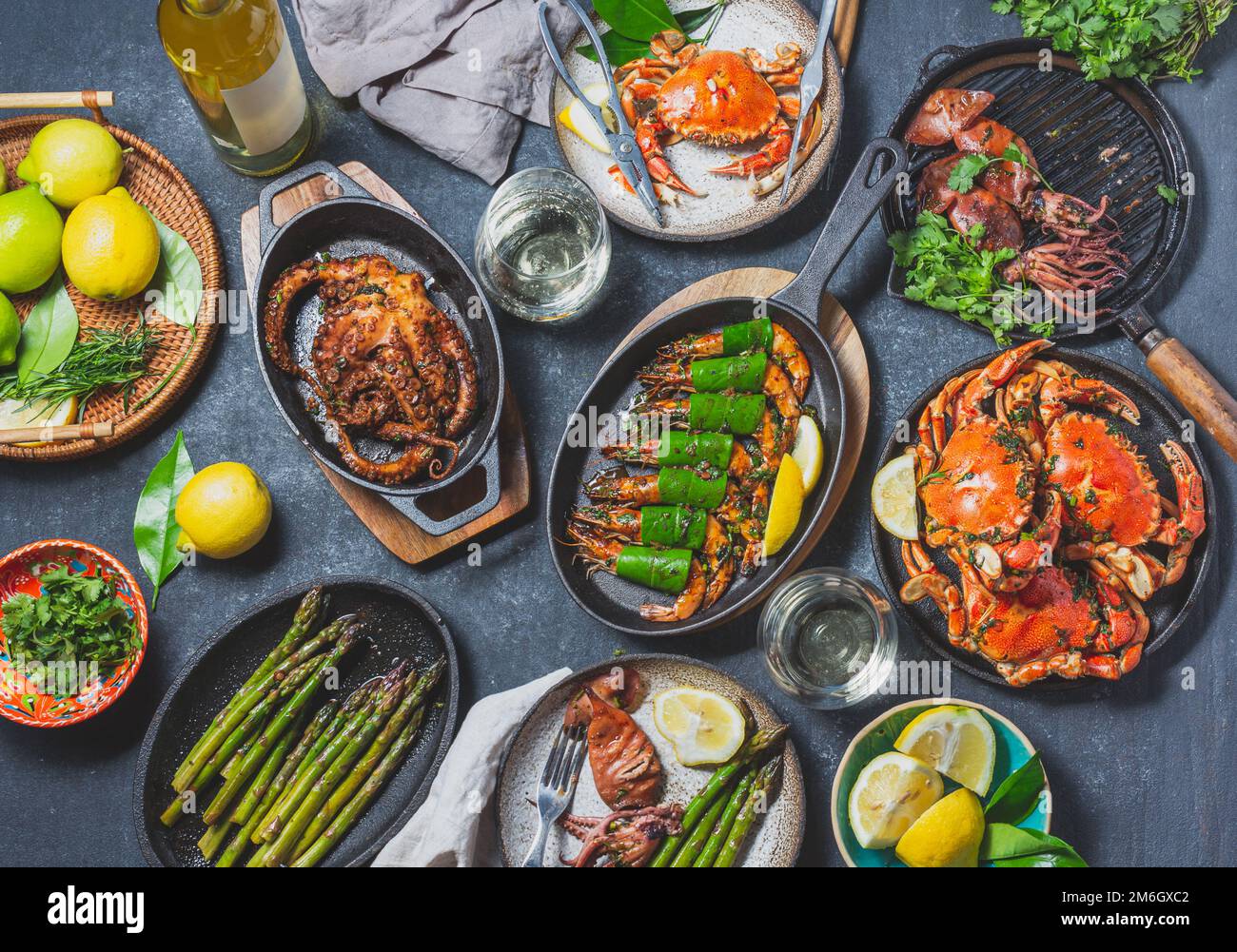 Set table con piatti di pesce - granchi cotti, gamberetti tigre, polpi alla griglia e calamari su padelle e piatti alla griglia in ghisa, vino bianco. Foto dai toni. Foto Stock