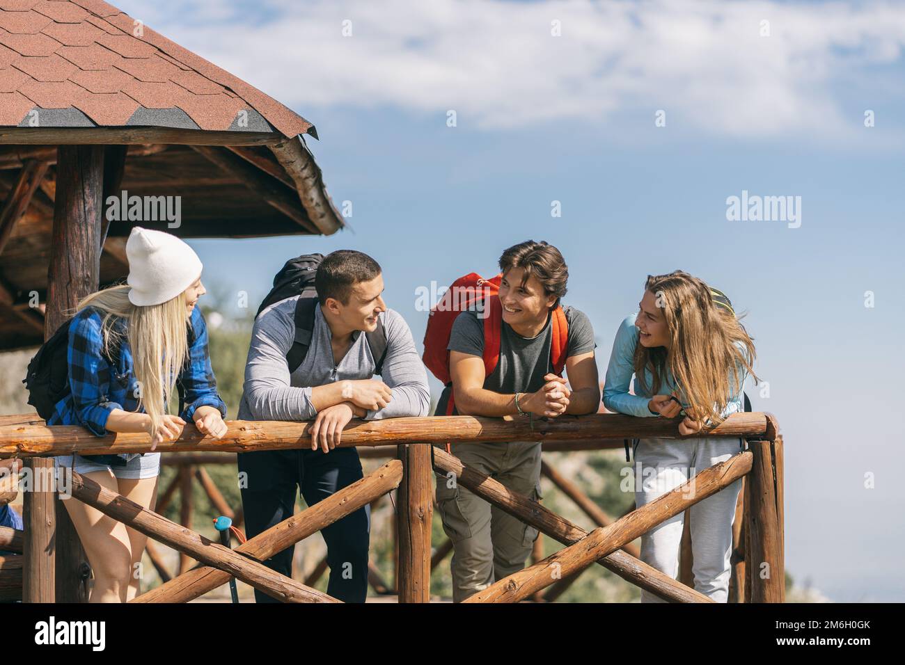 Quattro amici sorridono e parlano appoggiandosi sulla panca di legno Foto Stock