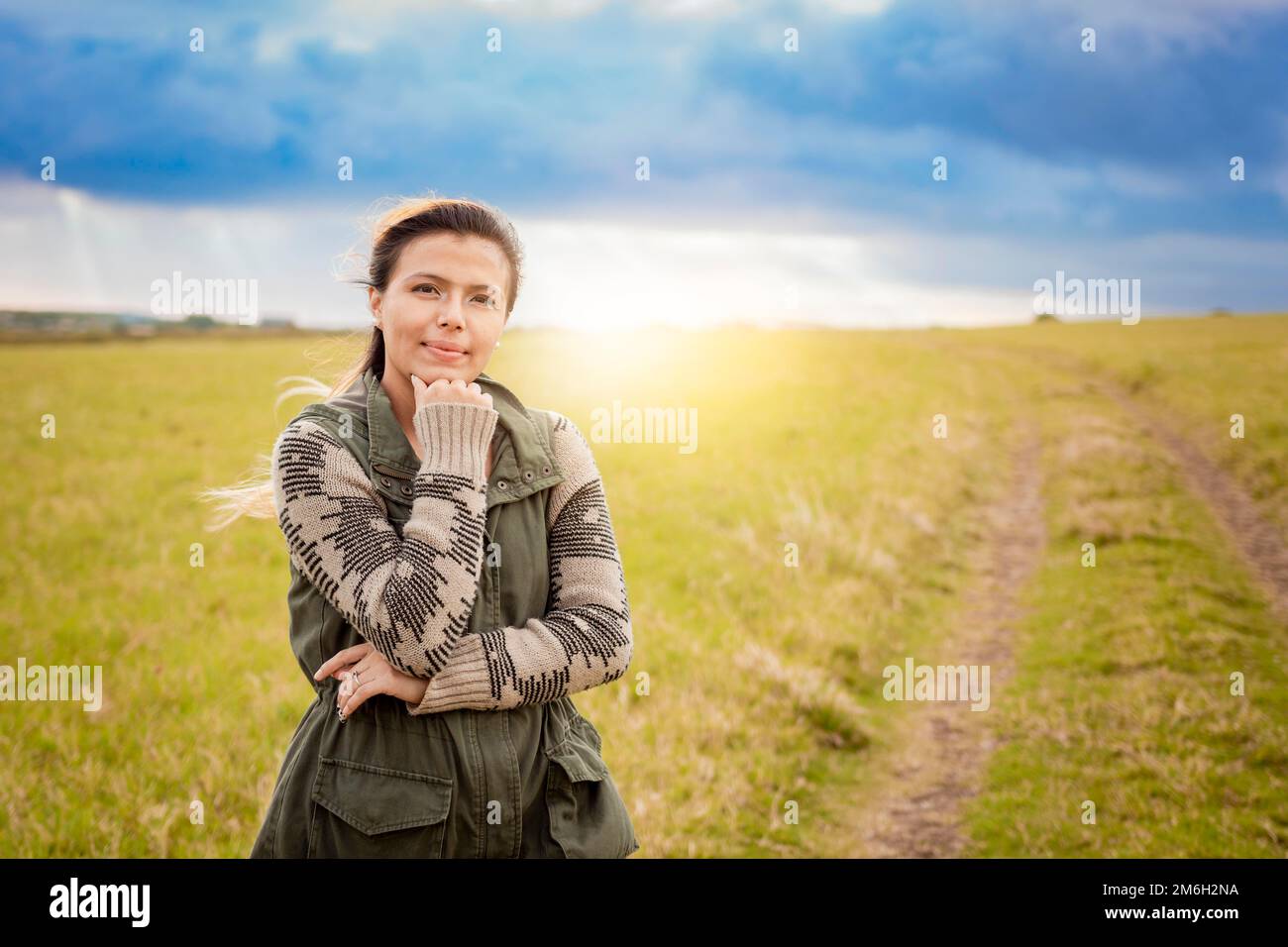 Una donna su un sentiero nella campagna tramonto. Ritratto di giovane donna con mano sul mento su una bella strada di campagna. Donna sorridente con mano sul mento Foto Stock