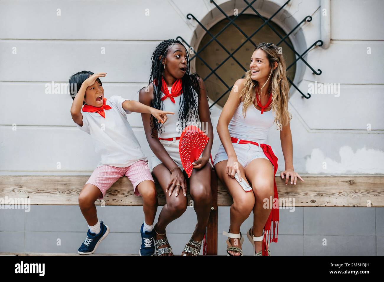 un ragazzo e due ragazze di diversa etnia, seduti su una barriera di legno, guardano con paura e sorpresa la corsa dei tori. Concetto di divertimento, Foto Stock