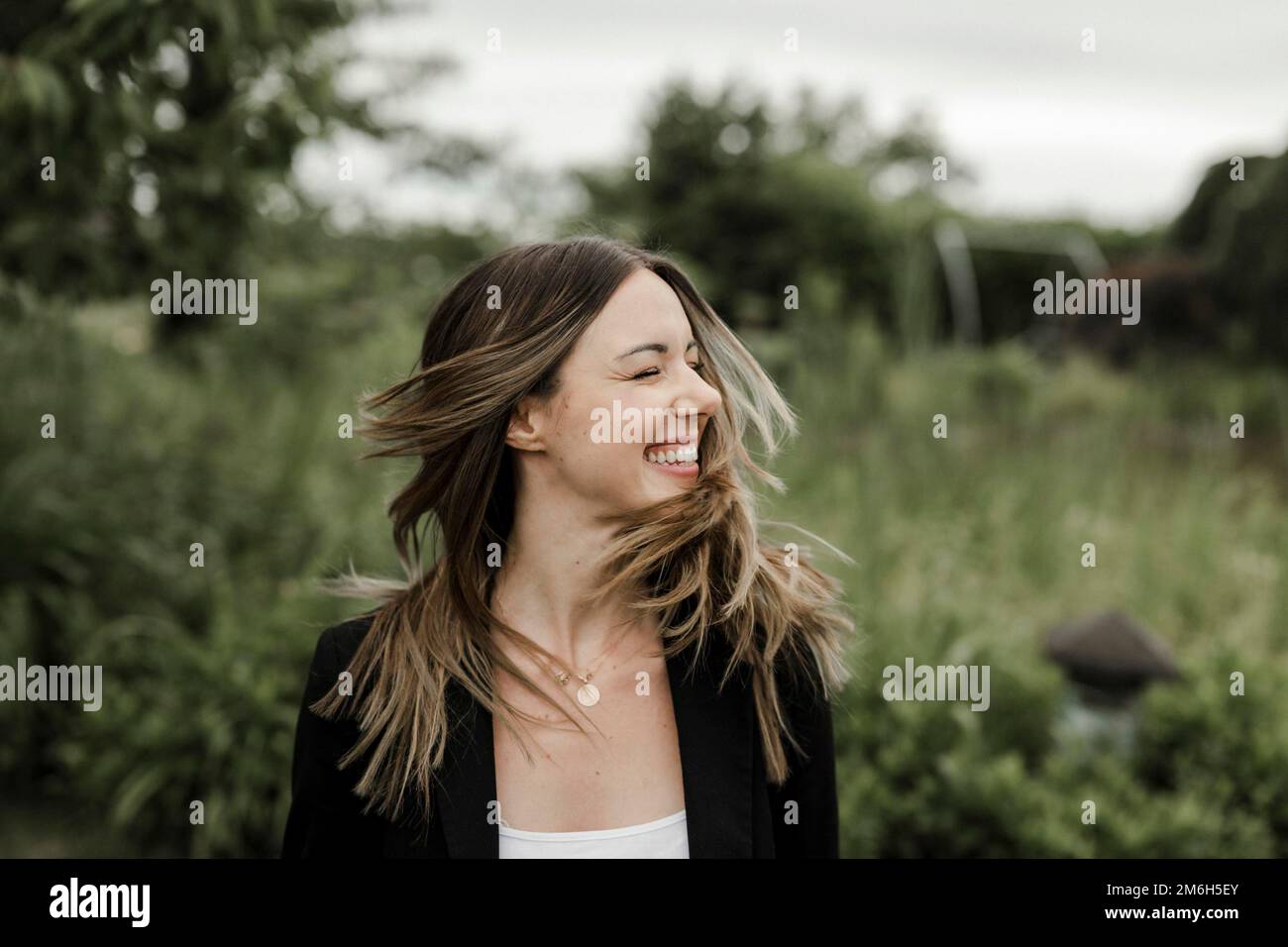 Giovane donna ridente in ritratto, 25, con capelli volanti Foto Stock