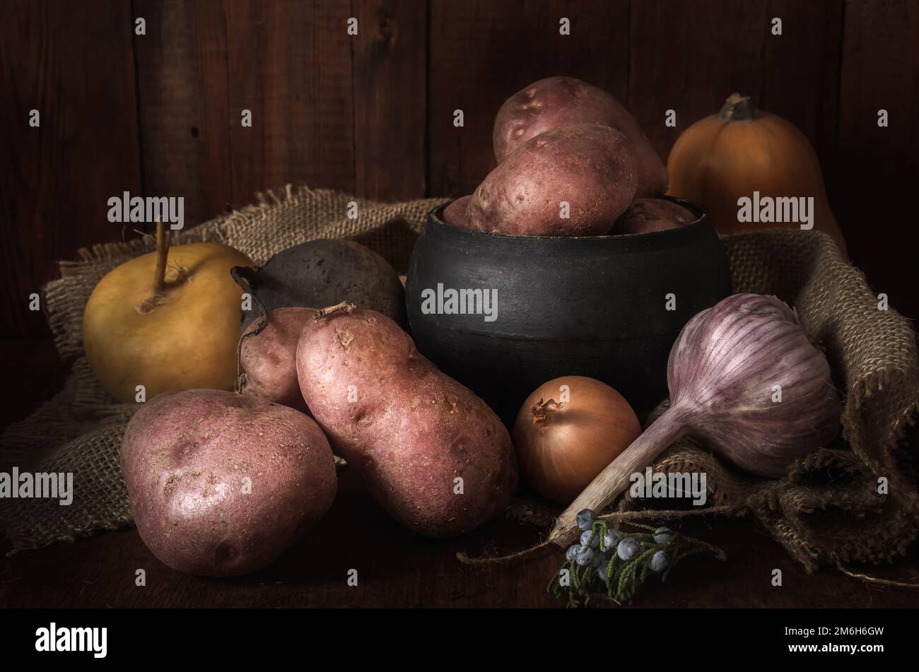 Tuberi di patate e altre verdure mature su sfondo di legno scuro in stile rustico Foto Stock