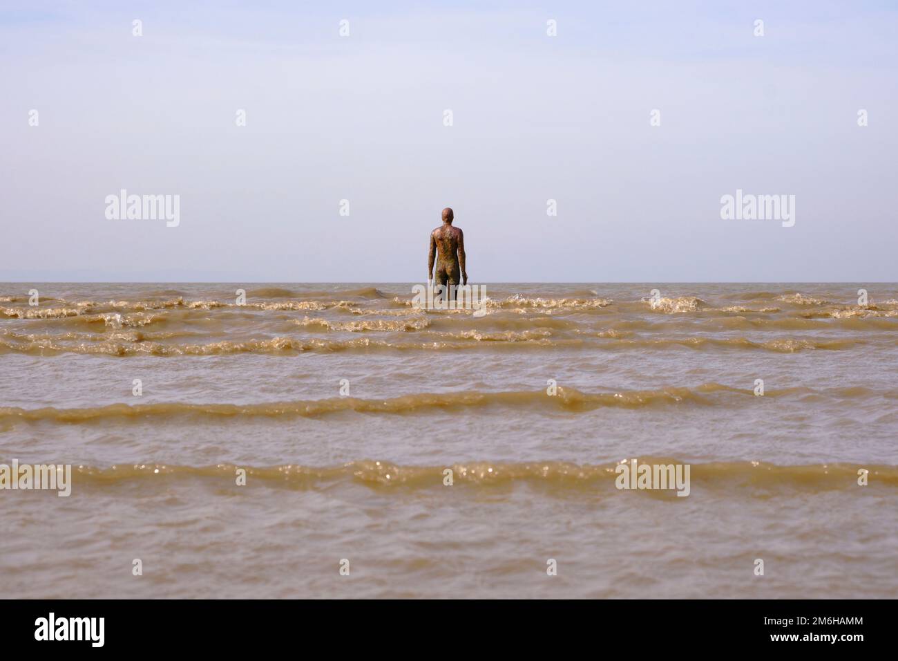 La marea si scontra con la scultura di Anthony Gormley, un altro luogo su Crosby Beach Foto Stock