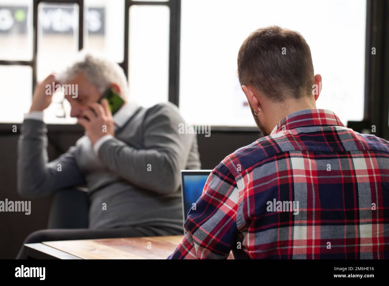 Situazione anonima con un ragazzo irriconoscibile, con la schiena girata mentre si utilizza il portatile e un uomo anziano fuori fuoco telefonando con h Foto Stock